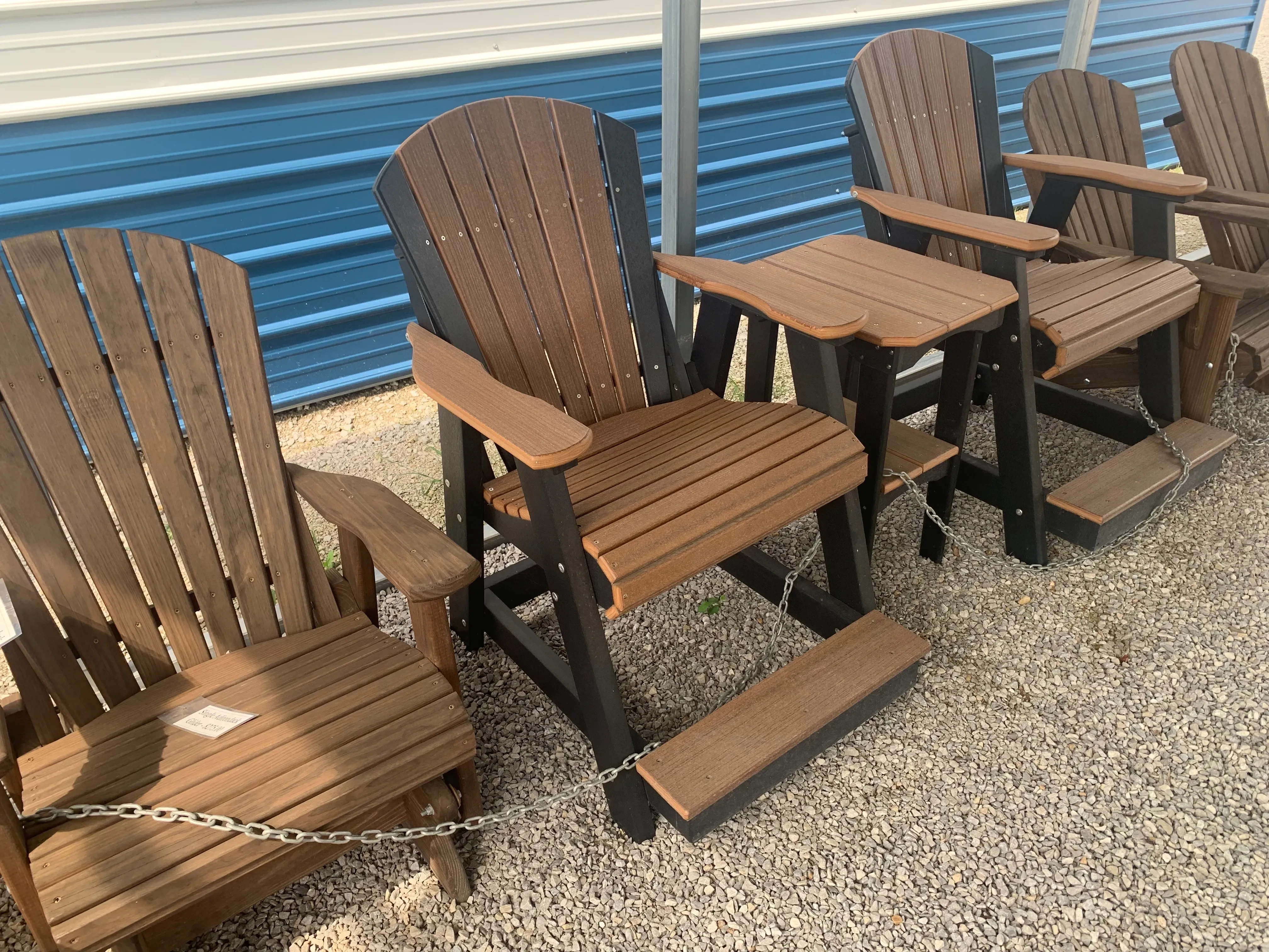 a chair sitting on the gravel. It is black and brown and made out of a polywood material.