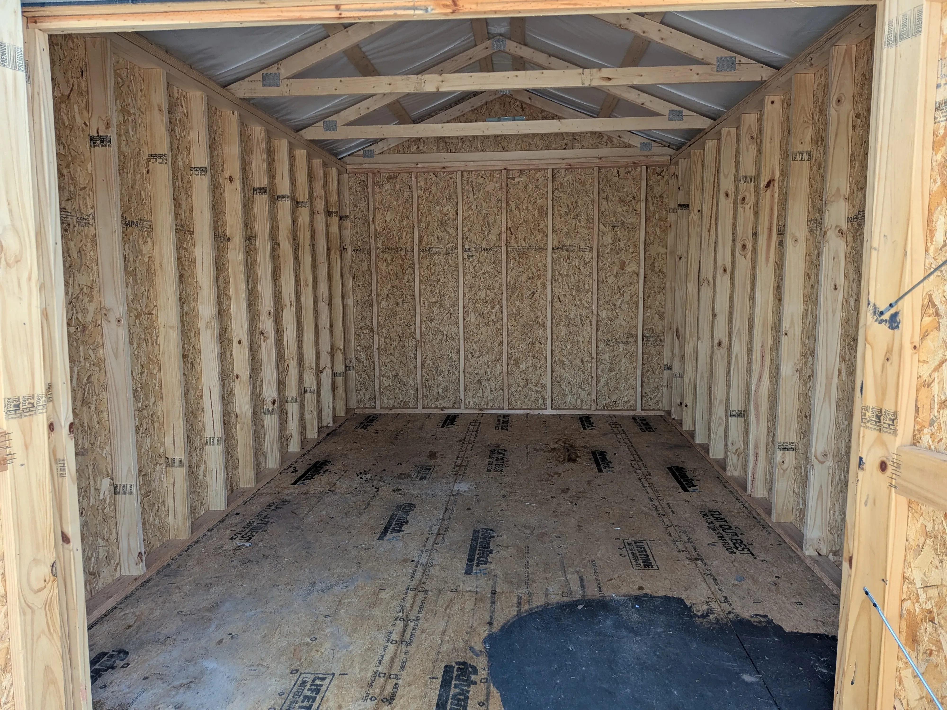 inside a wood utility shed looking at the back wall. There is a large black stain on the floorboard