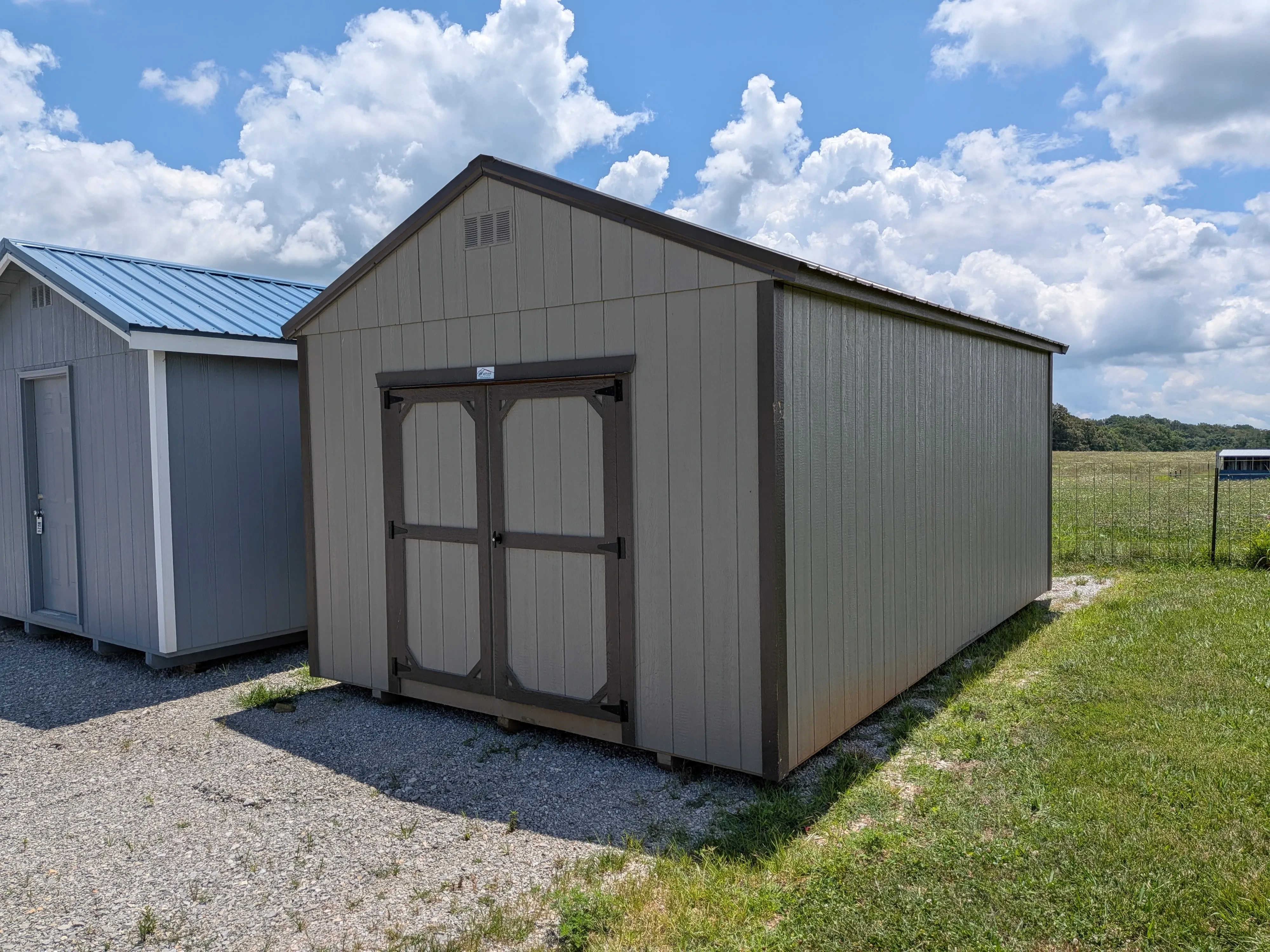 a large wood utility shed with double doors in the front. It is clay colored with bronze trim and a bronze roof