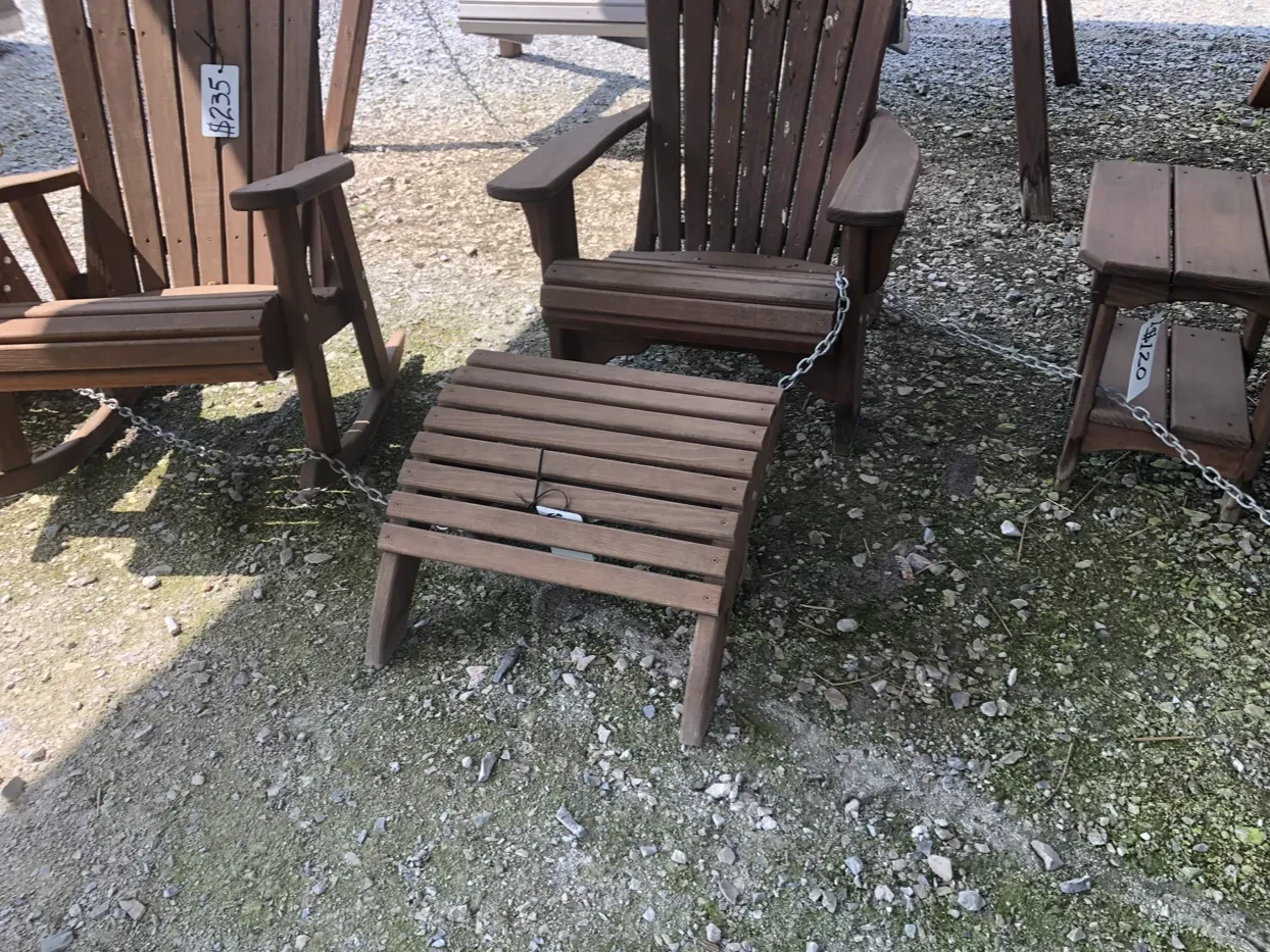 a wood stained and sealed footstool sitting on gravel next to chairs