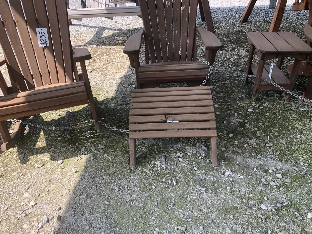 a stained and sealed wood foot stool sitting next to other chairs and on gravel