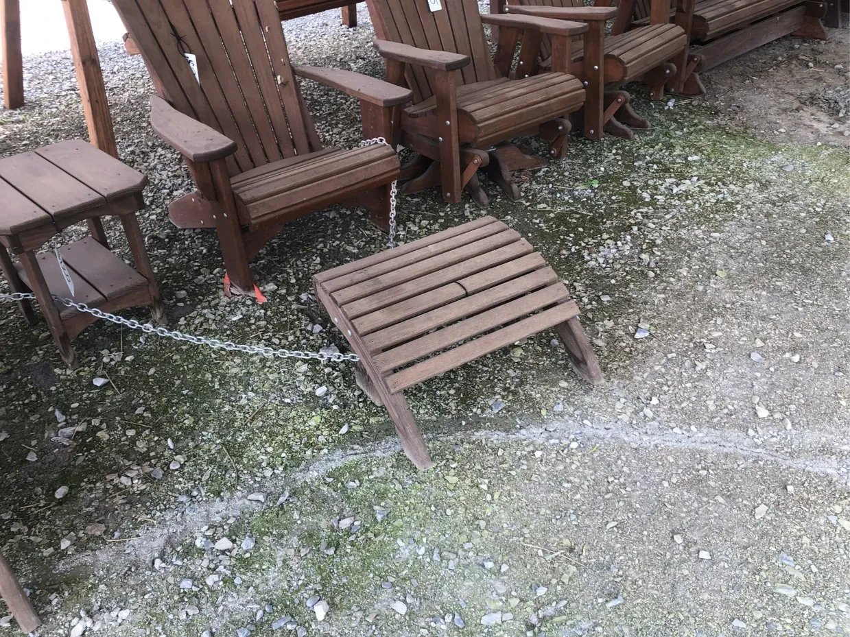 a wood stained and sealed footstool sitting on gravel next to other wood chairs