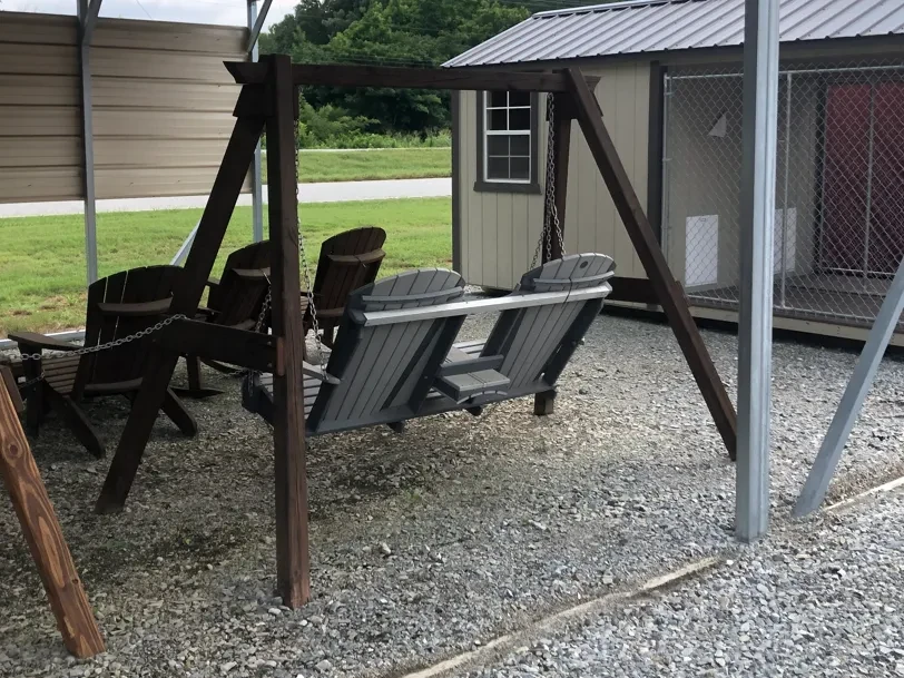 an a-frame structure made out of wood, it is holding up a swing made out of polywood over gravel