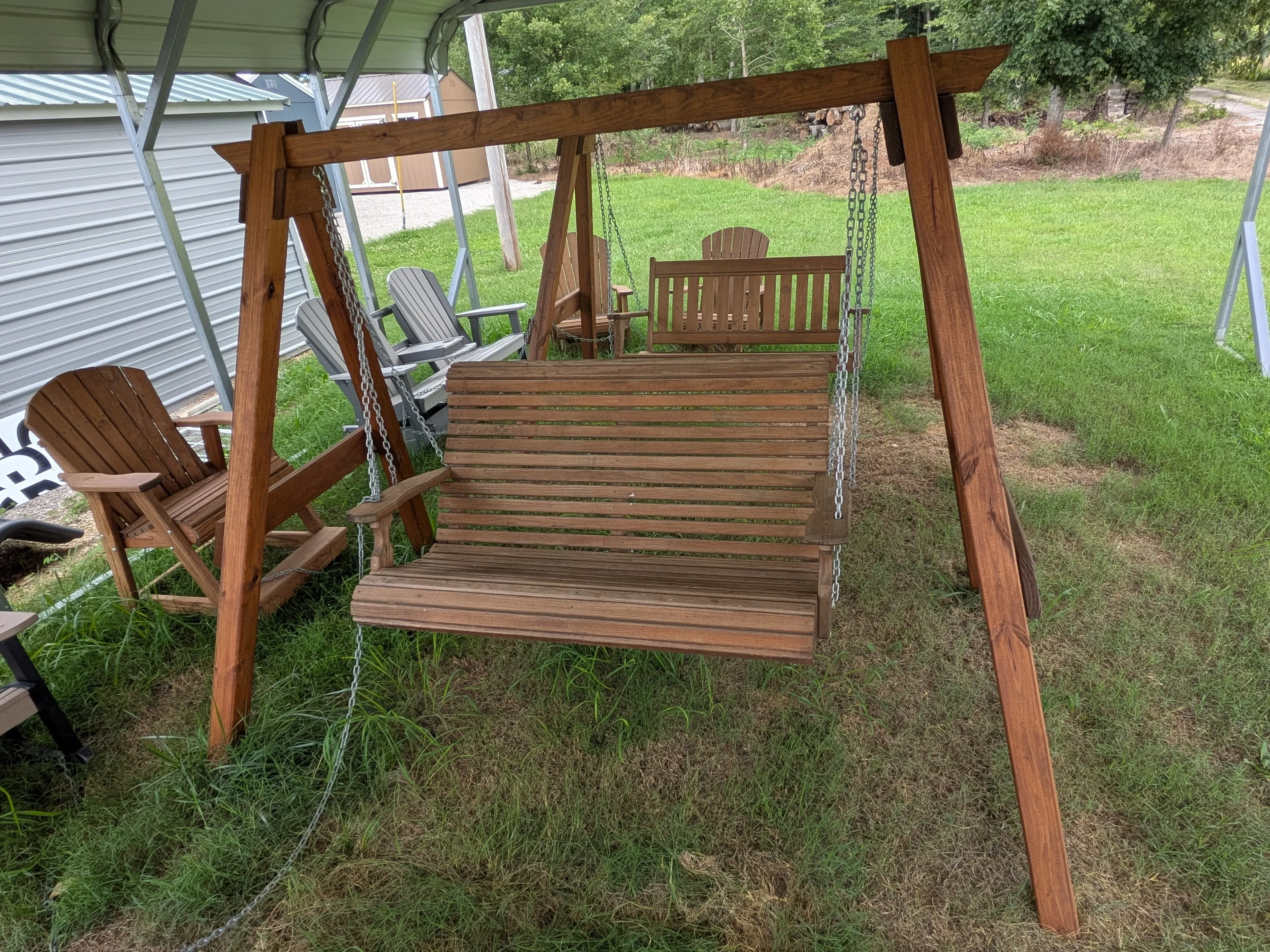 a wooden swing held up by a wooden stained and sealed a-frame structure in the grass next to other furniture
