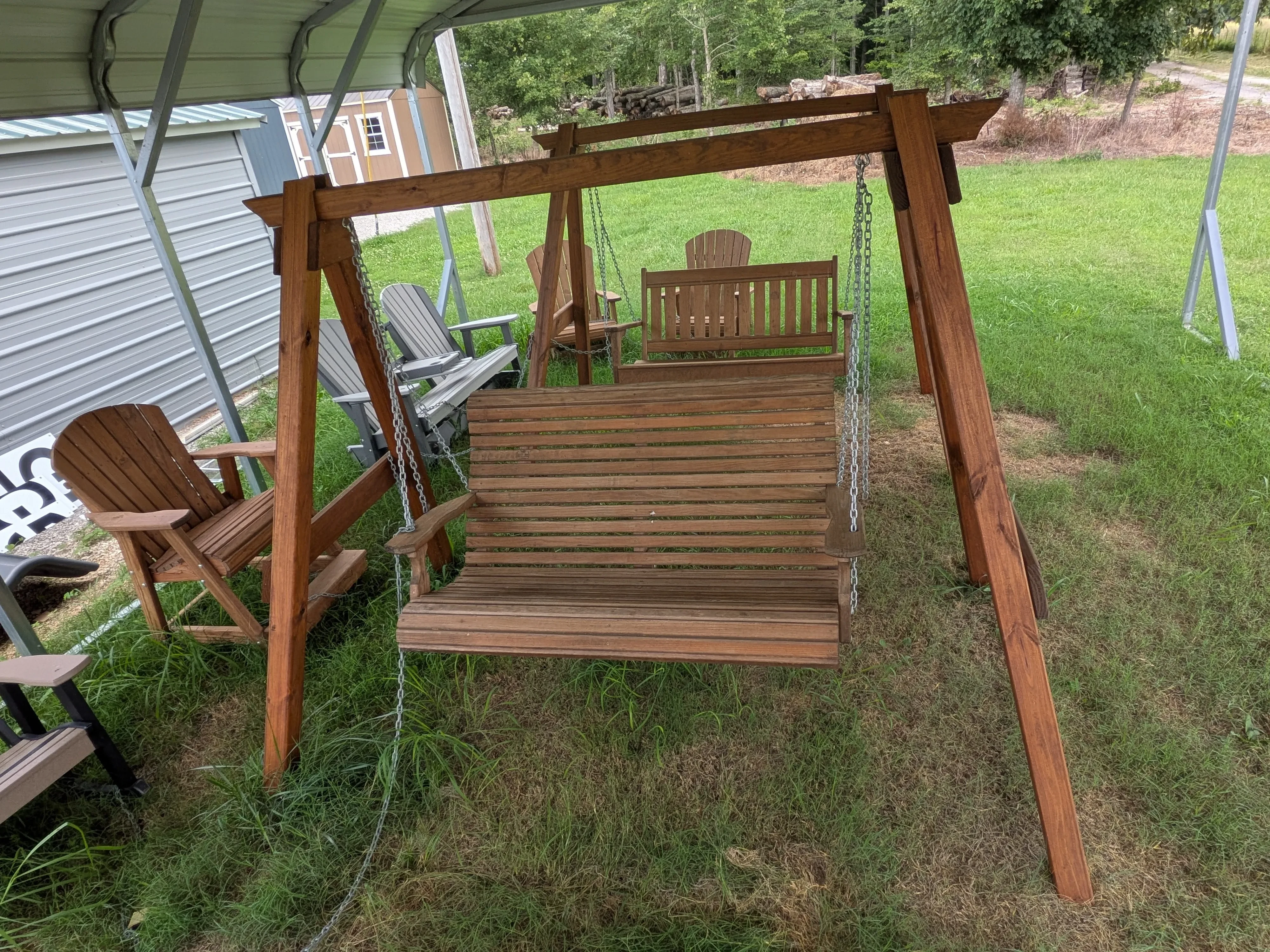 a wooden a-frame structure holding up a wooden swing over grass next to other furniture