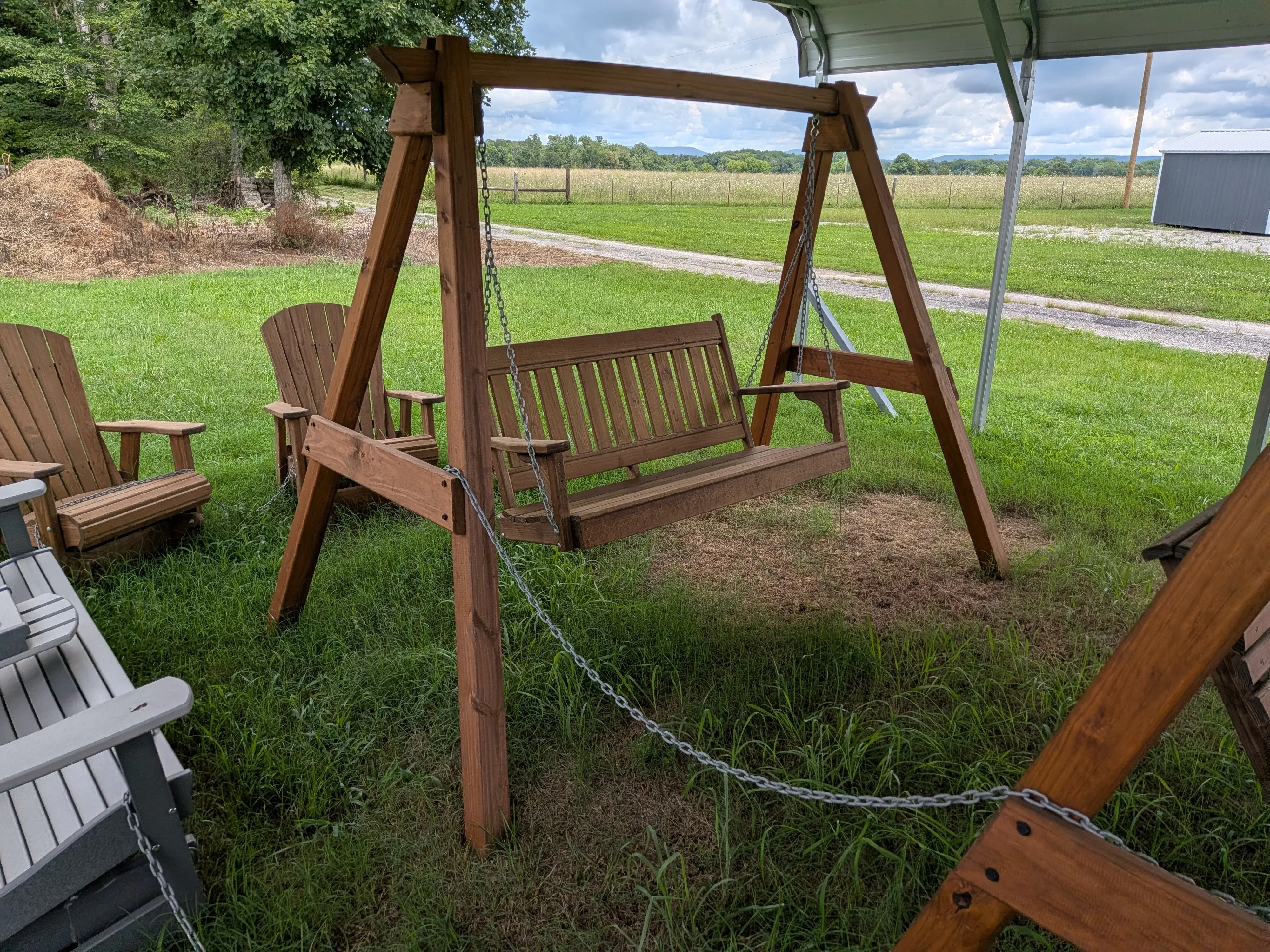 a wooden stained and sealed a-frame structure holding up a wooden swing in the grass near other furniture