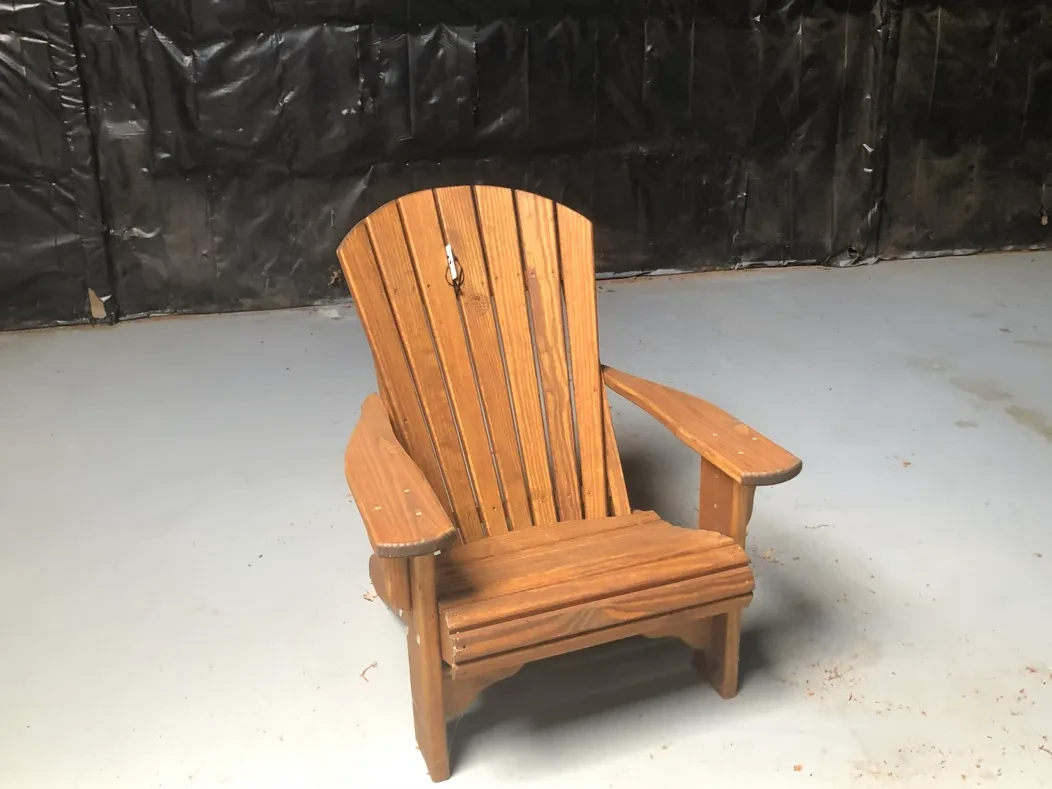 a wood stained and sealed chair sitting in a room by itself. The wall behind it is black