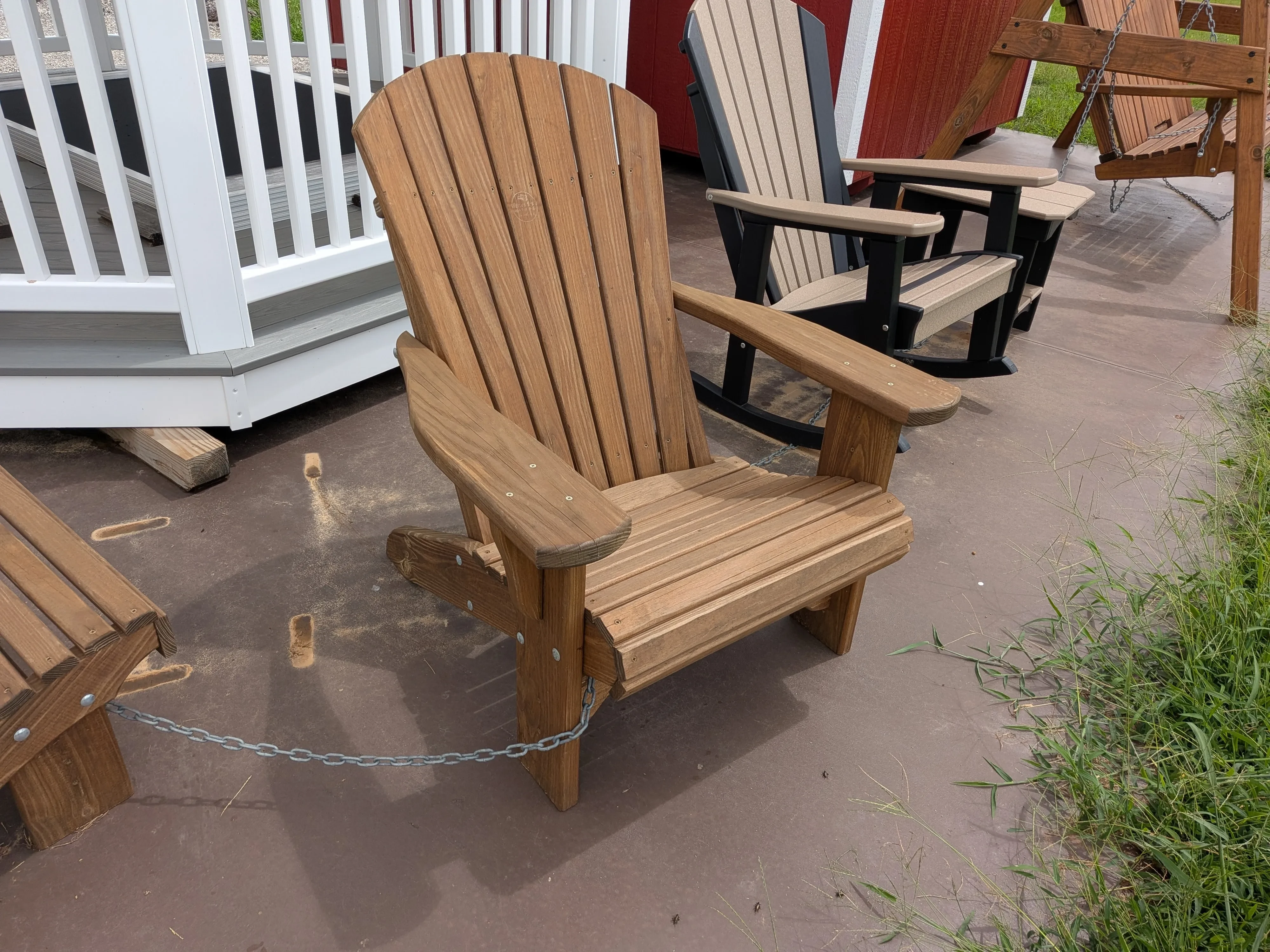 a wood stained and sealed chair sitting on a concrete pad. It is chained up to other furniture nearby