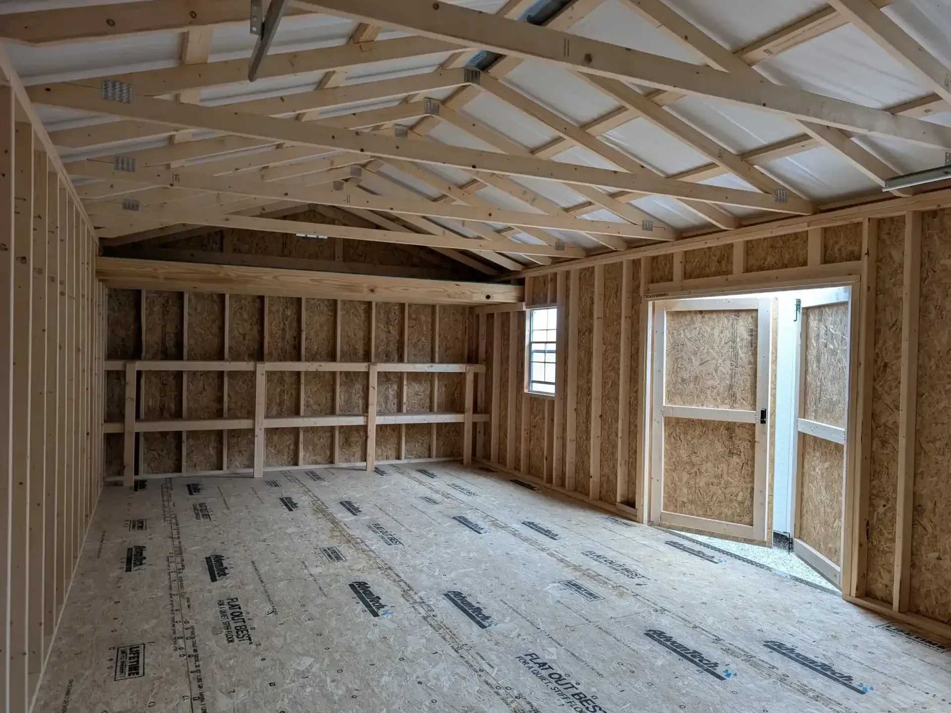 The inside of a garage shed showing the double doors open as well as double shelves and a loft along the back wall