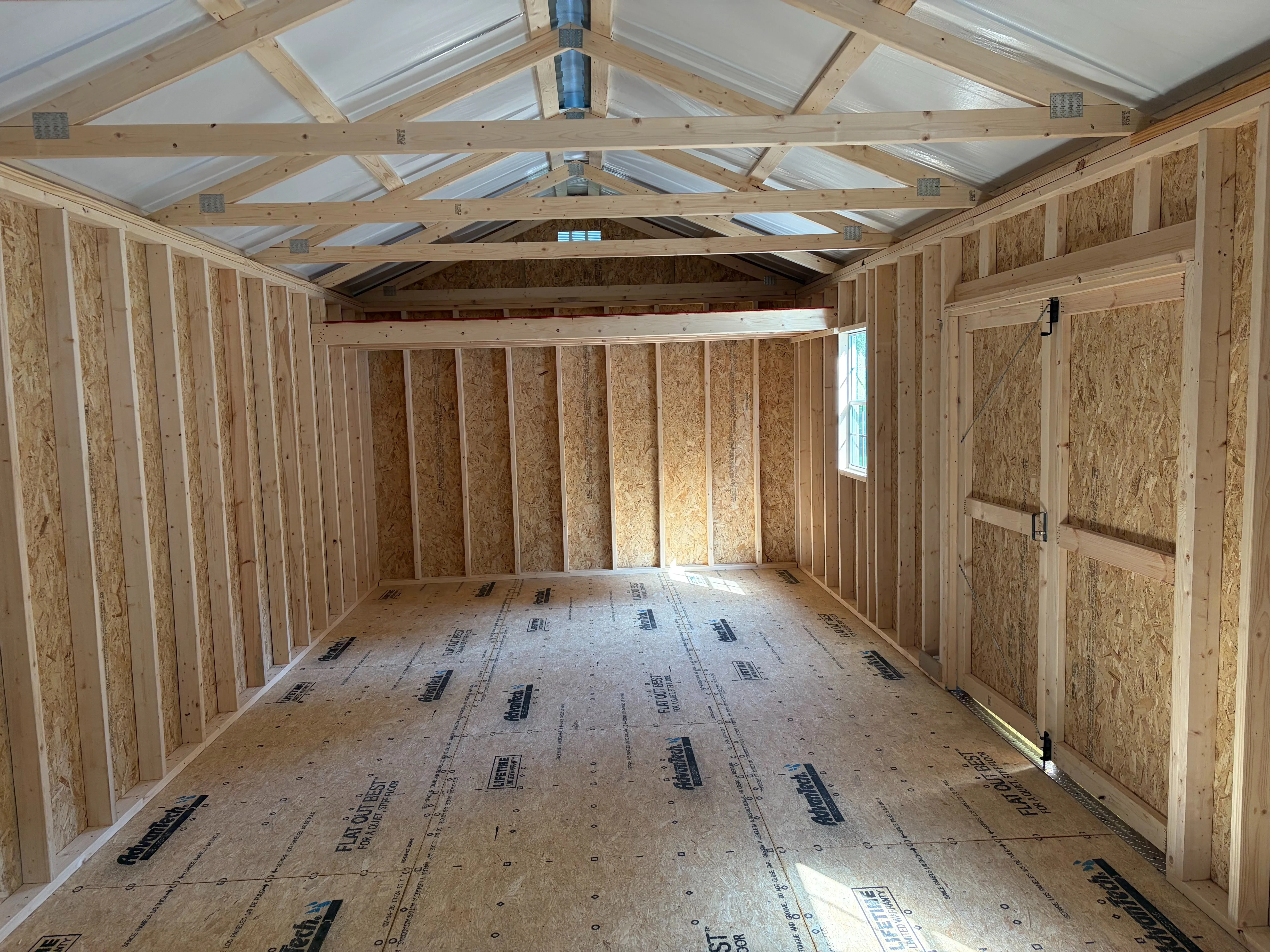 looking through the open rollup garage door into a wood garage shed, multiple windows, a loft, and closed double doors
