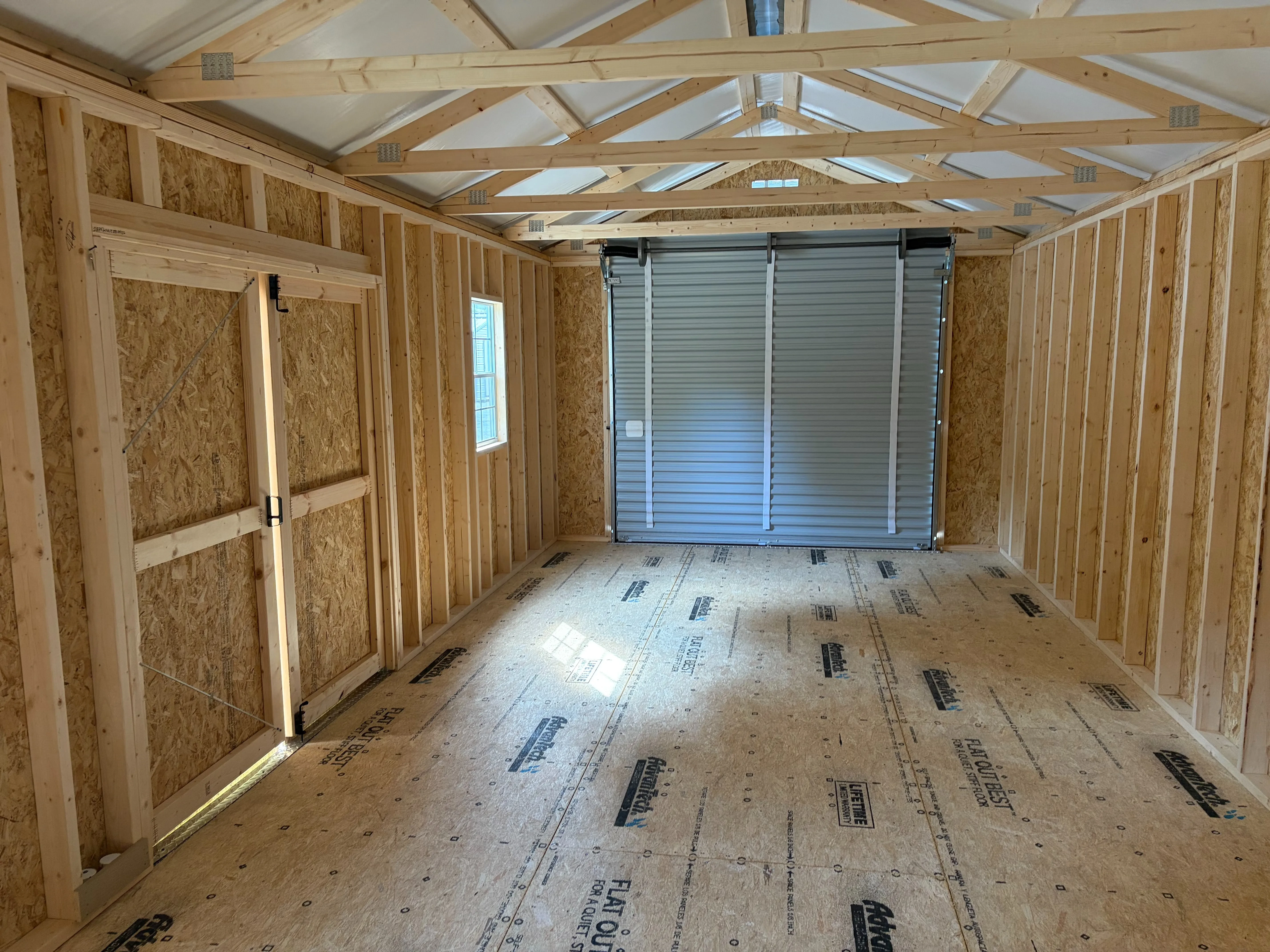 Inside large garage shed with rollup door closed and sun shining through windows
