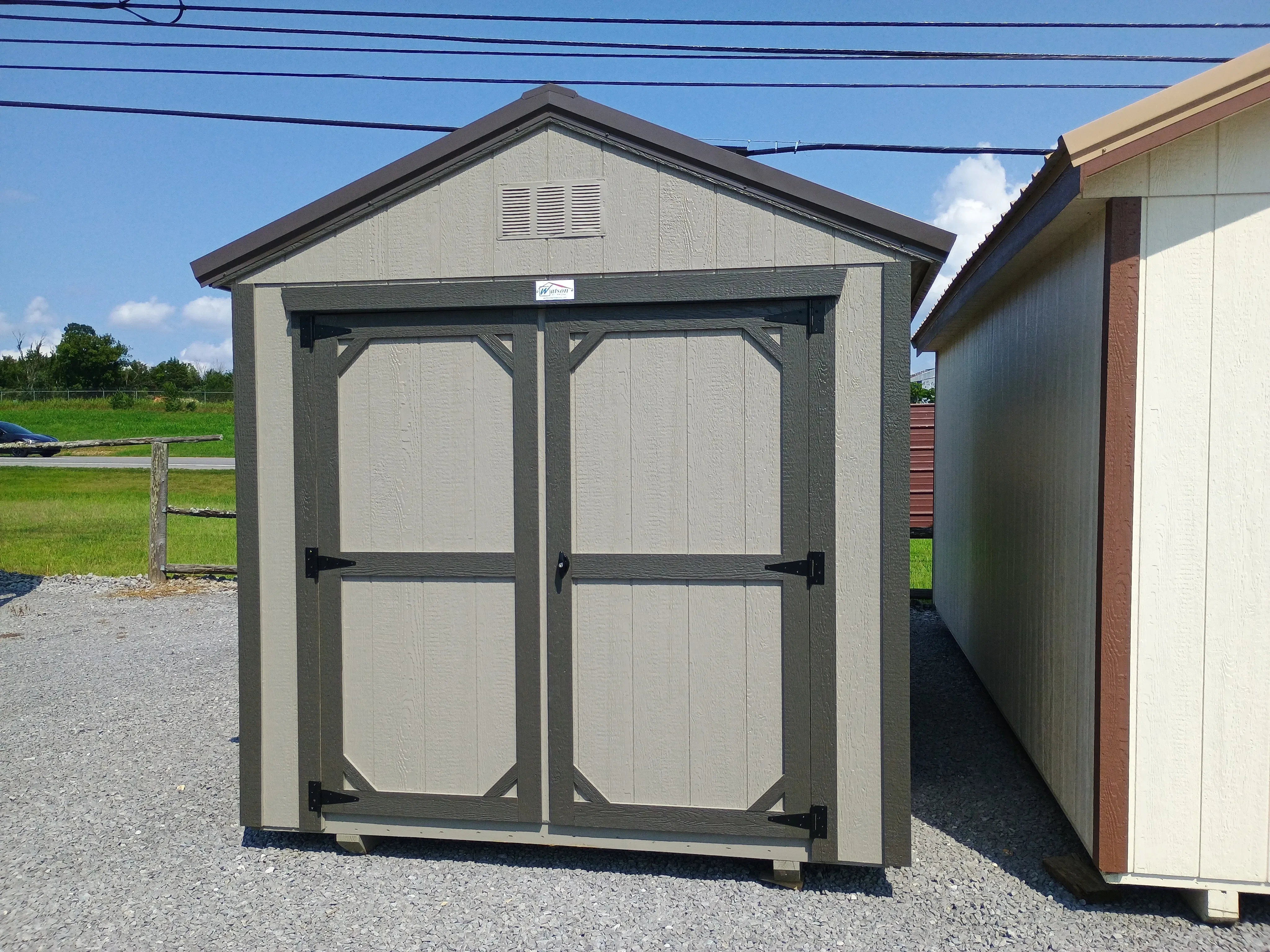 Outside of 8x12 utility shed with double doors on the end, with painted wood and metal roof.