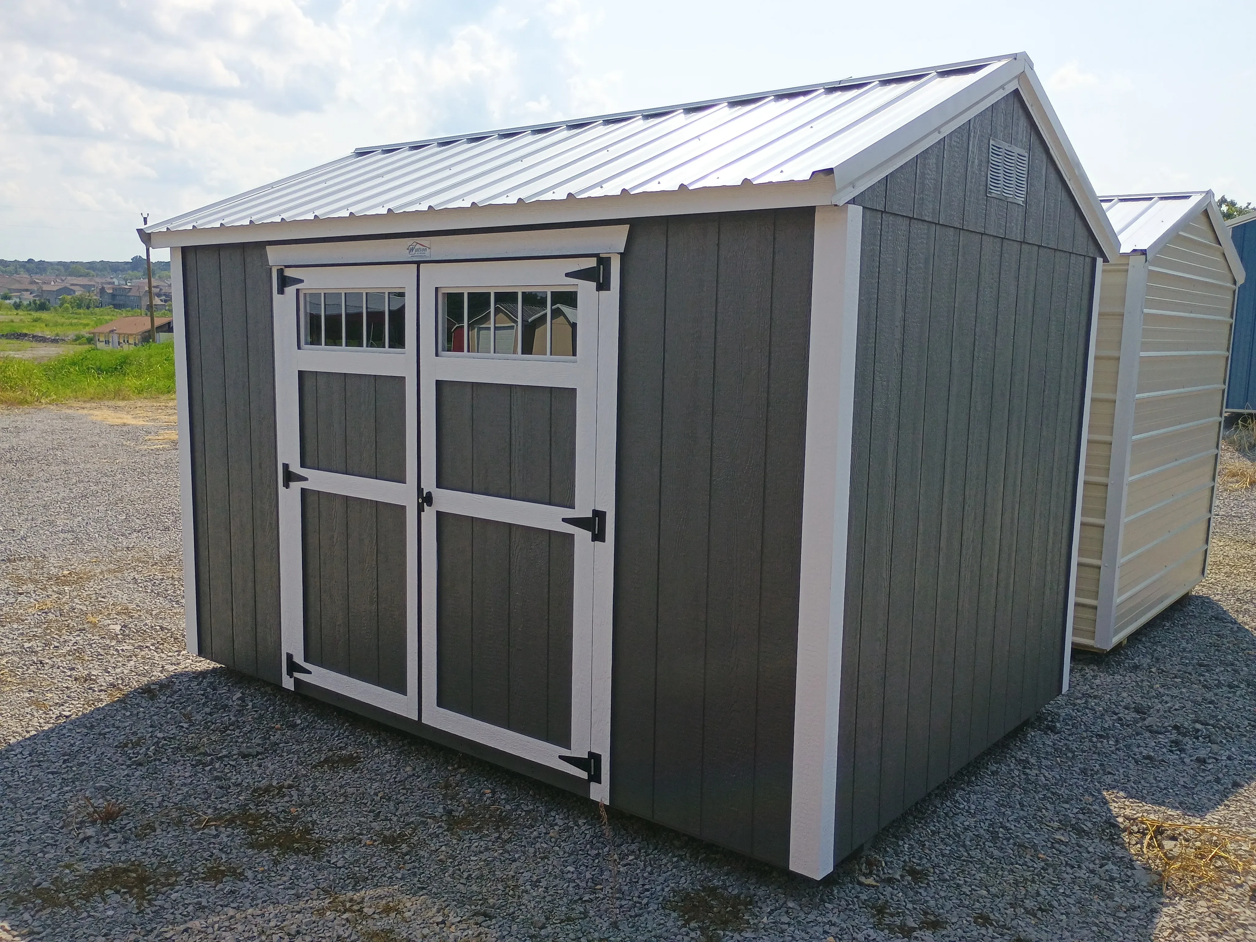 Outside of 8x12 wood garden shed with transom windows on double doors, painted and with metal roof.