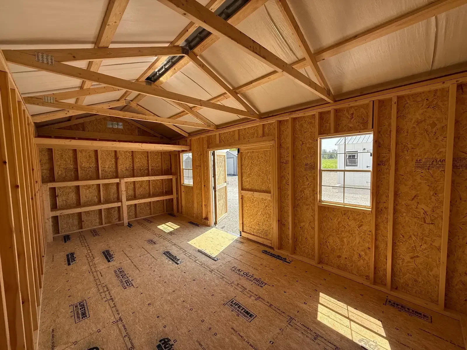 The inside of a 10x20 garden shed with double doors and two windows in the side and a loft and double shelves across the end