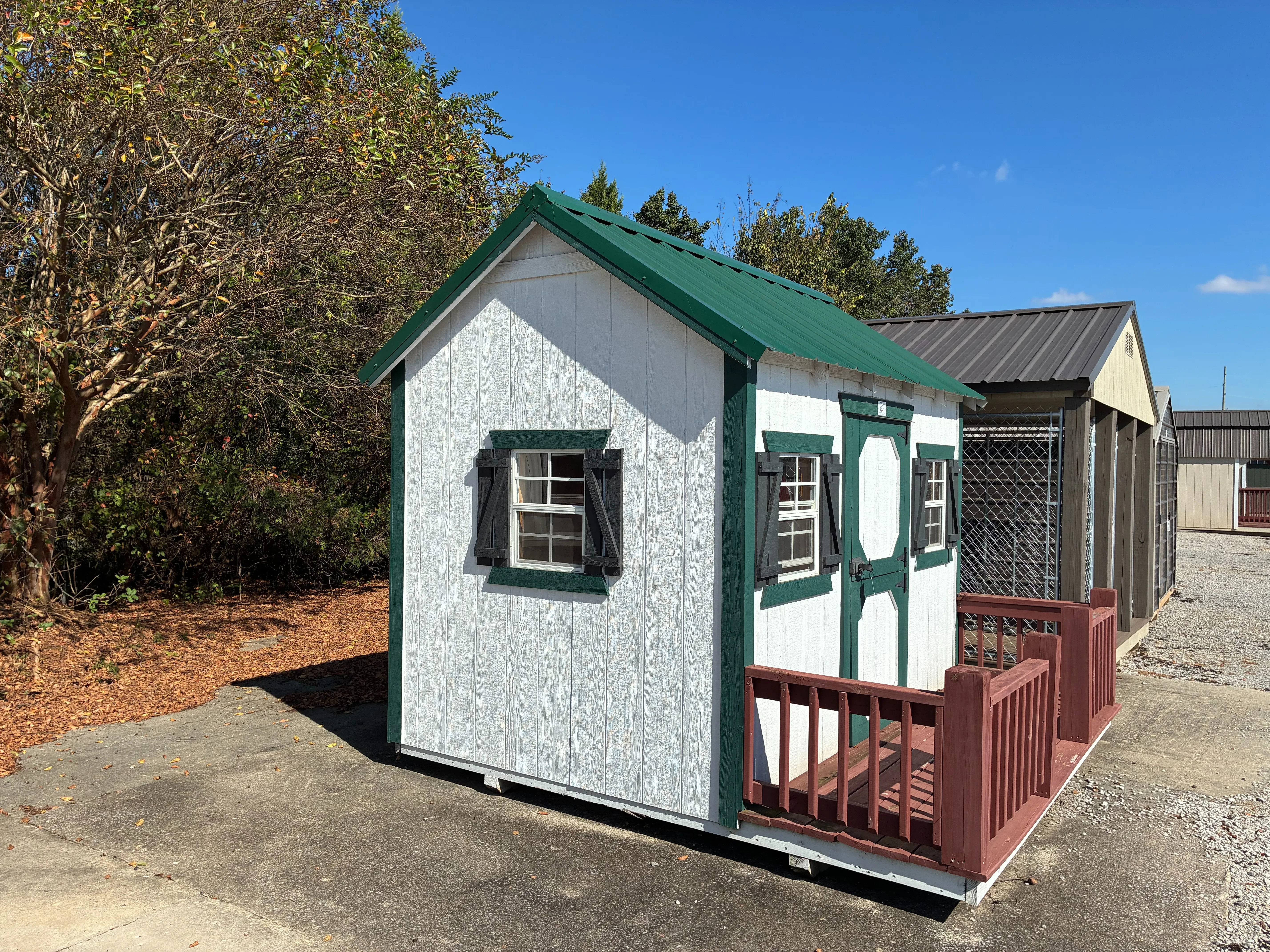 A 10x10 wood playhouse painted white with green trim. It has windows with green shutters and a small porch.