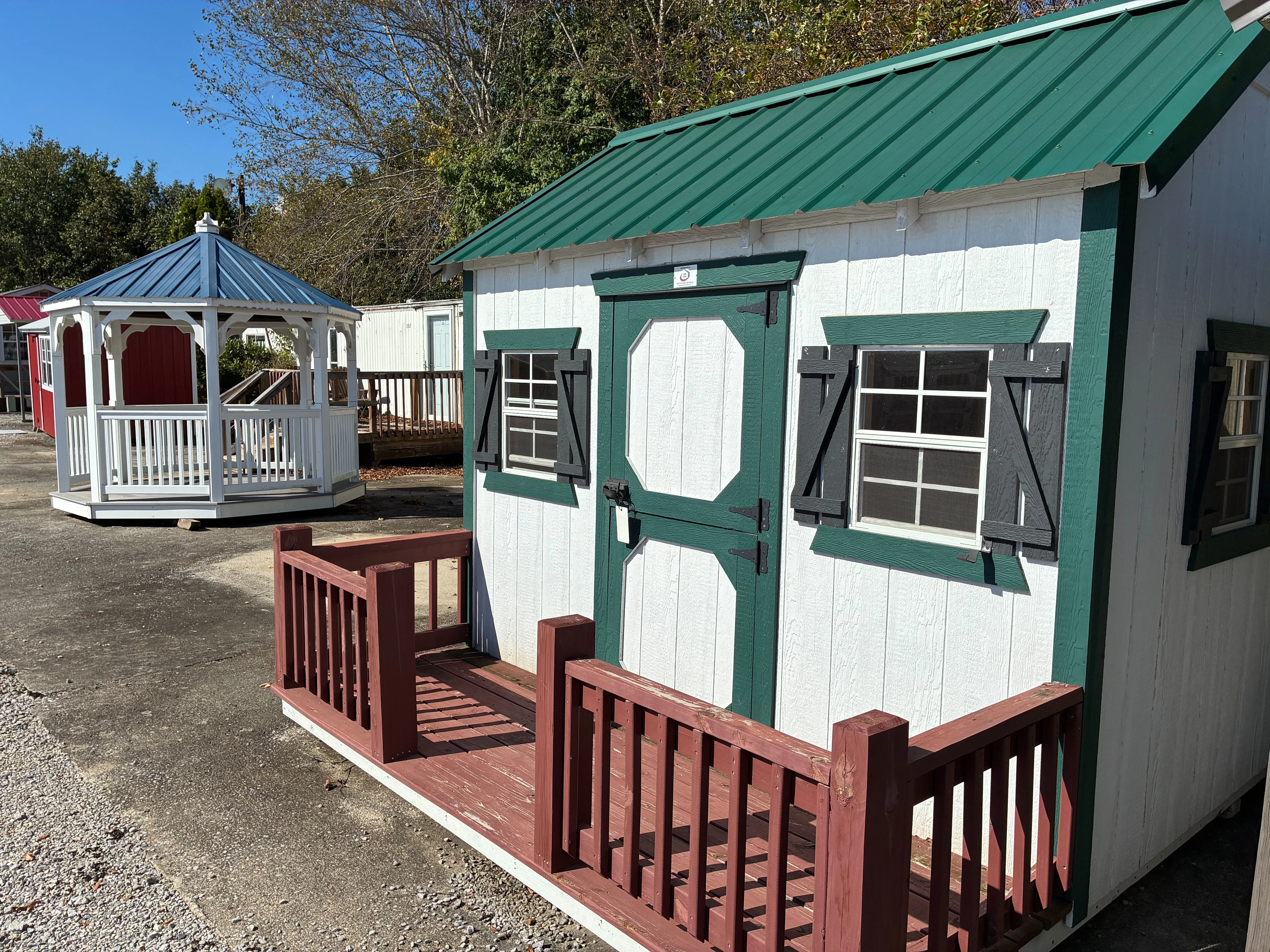 A 10x10 wood playhouse painted white with green trim. It has windows with green shutters and a small porch.