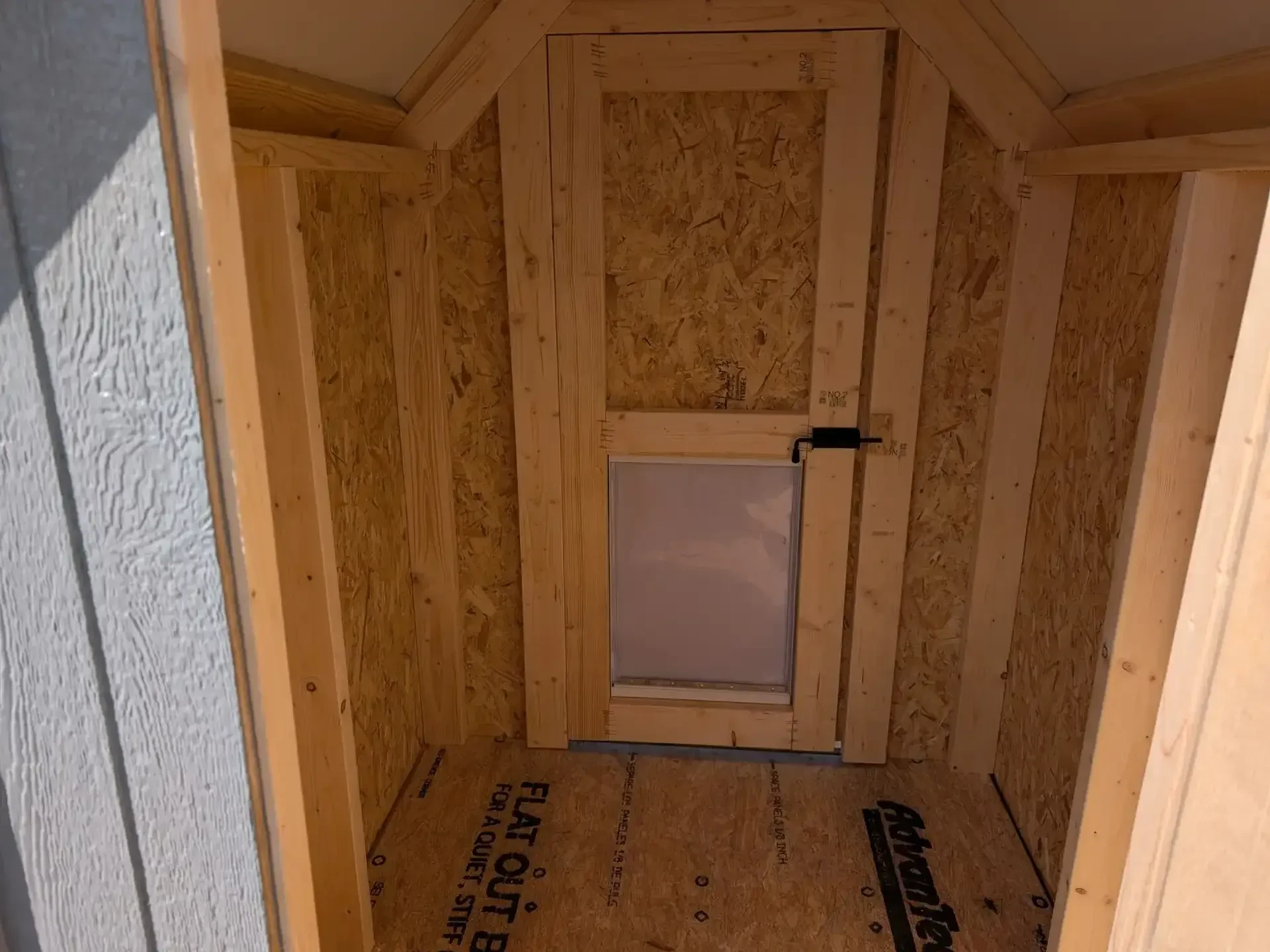 The inside of a wood dog kennel showing a doggy door