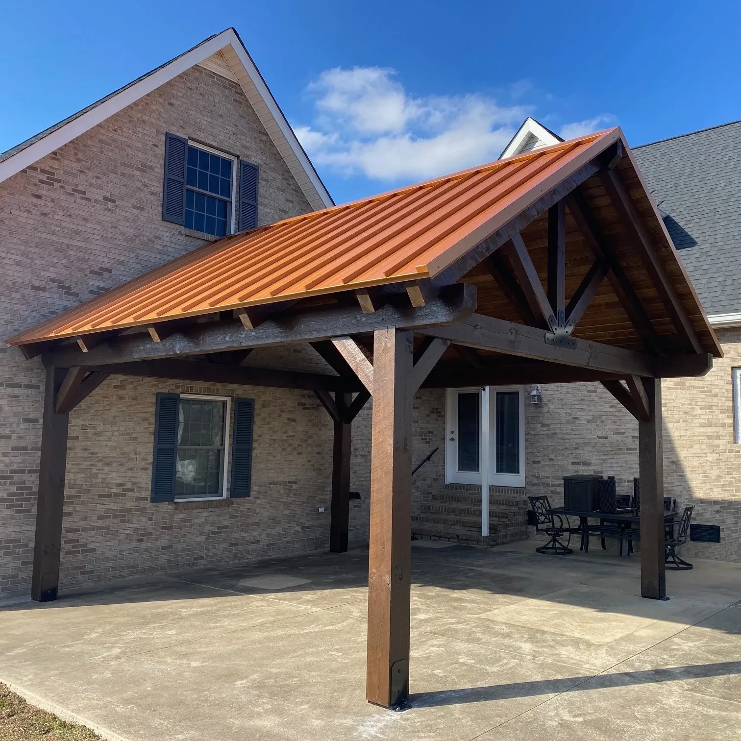 a classy timber frame pavilion with dark stained posts and rafters and a copper roof