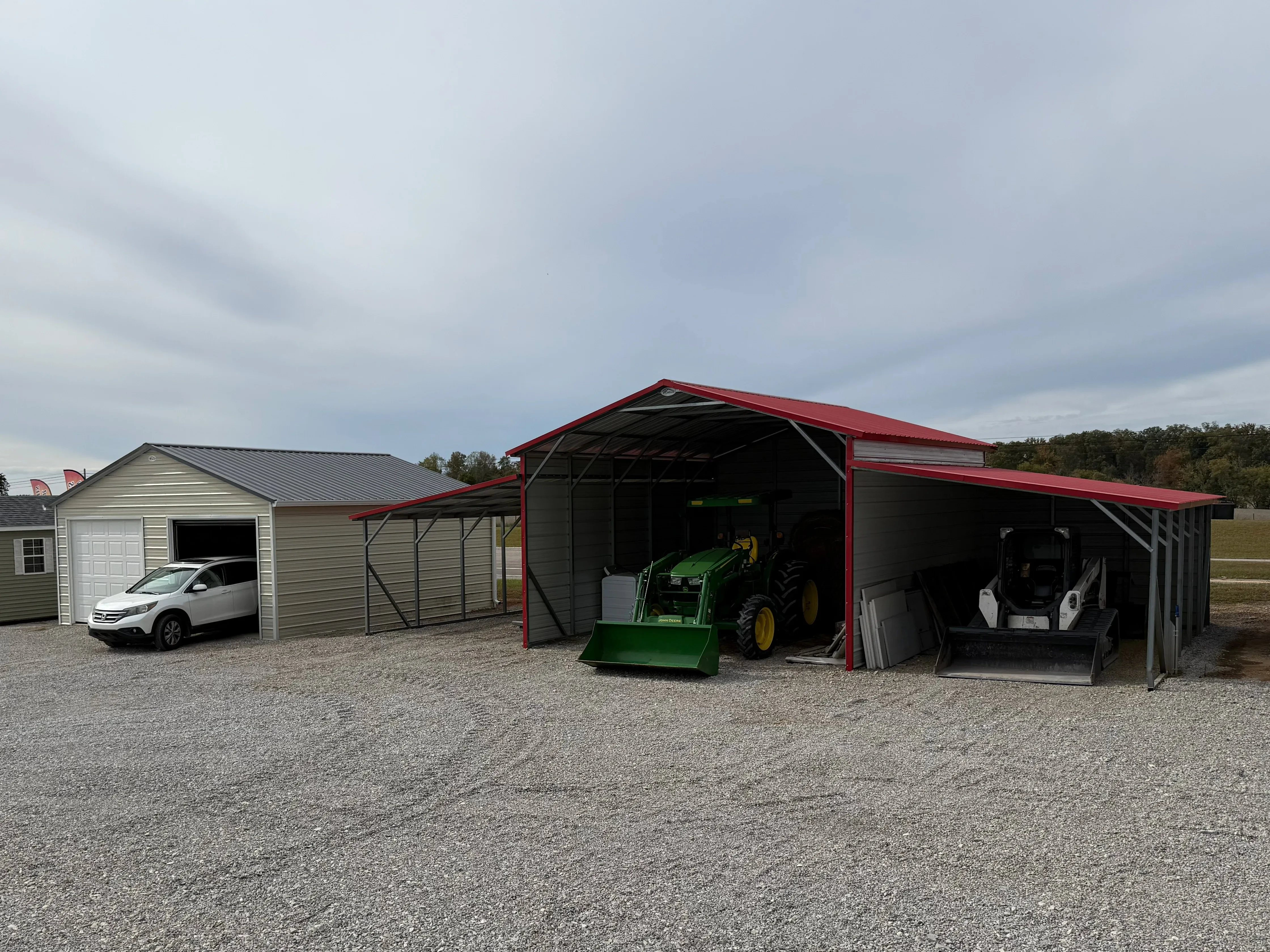a tennessee barn carport with equipment parked under it and a two car garage