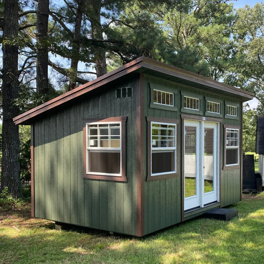 A forest green and brown studio shed with patio doors and many windows