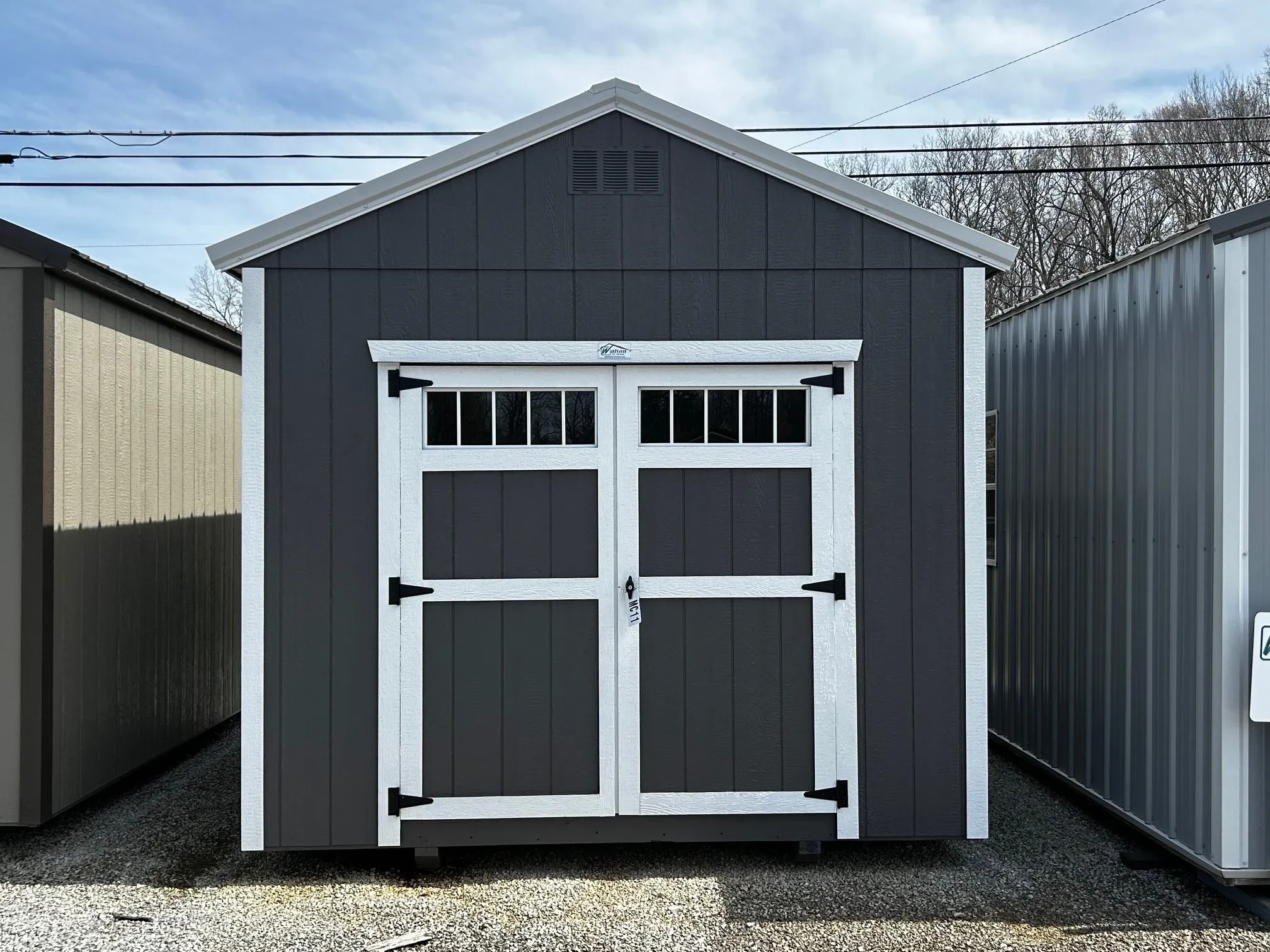 The front of a wood shed colored gray that has transom windows on the double doors