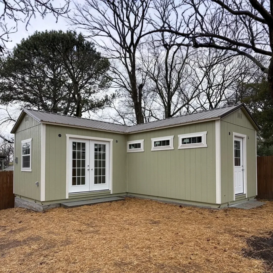 a custom light green L-Shaped shed with patio doors a 9-lite door, and multiple windows