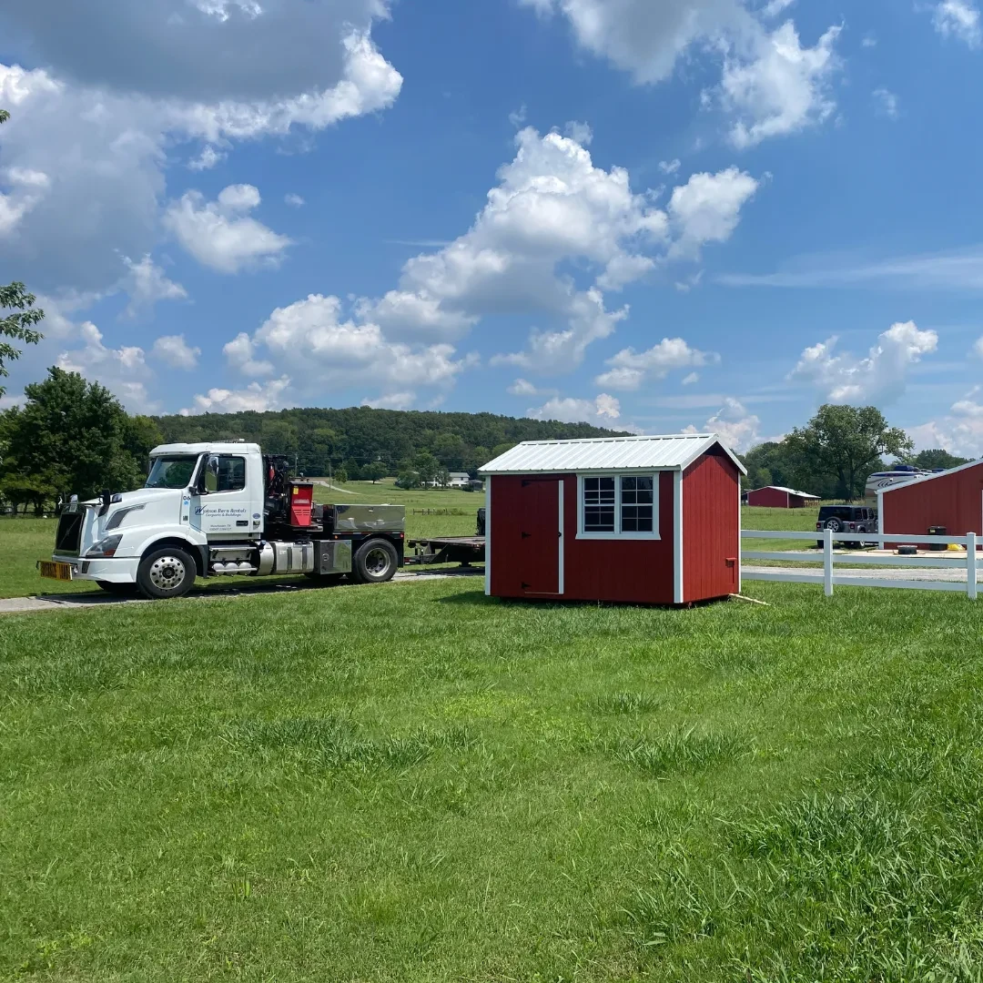 A small red chicken coop shed in the process of being delivered