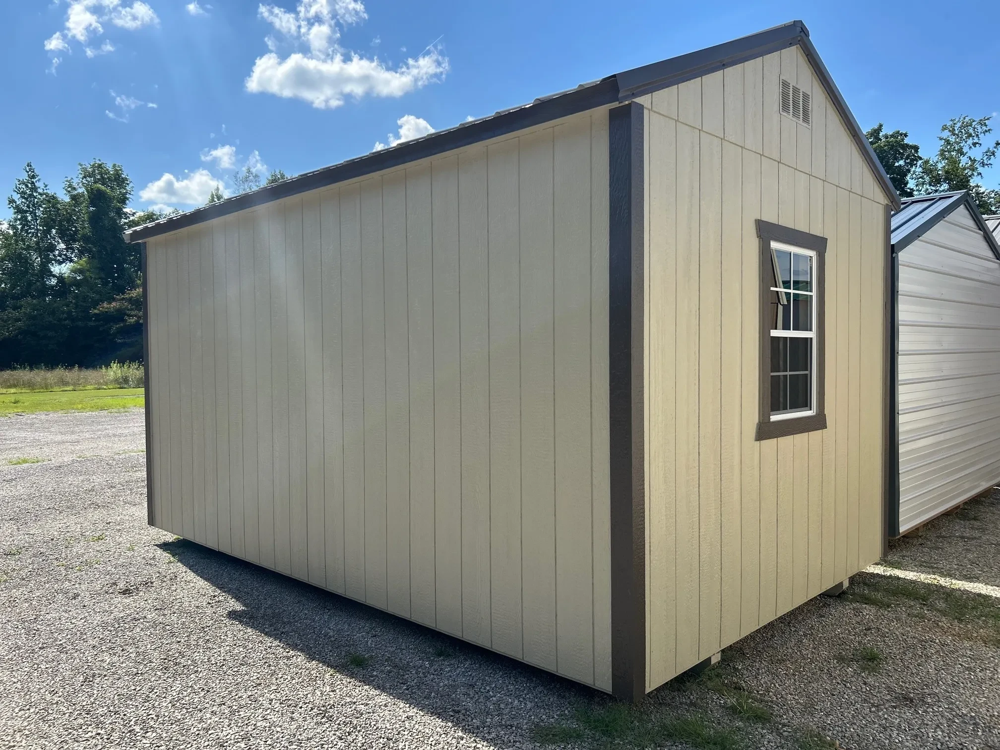 The side corner view of a light stone colored shed with a window in the back wall