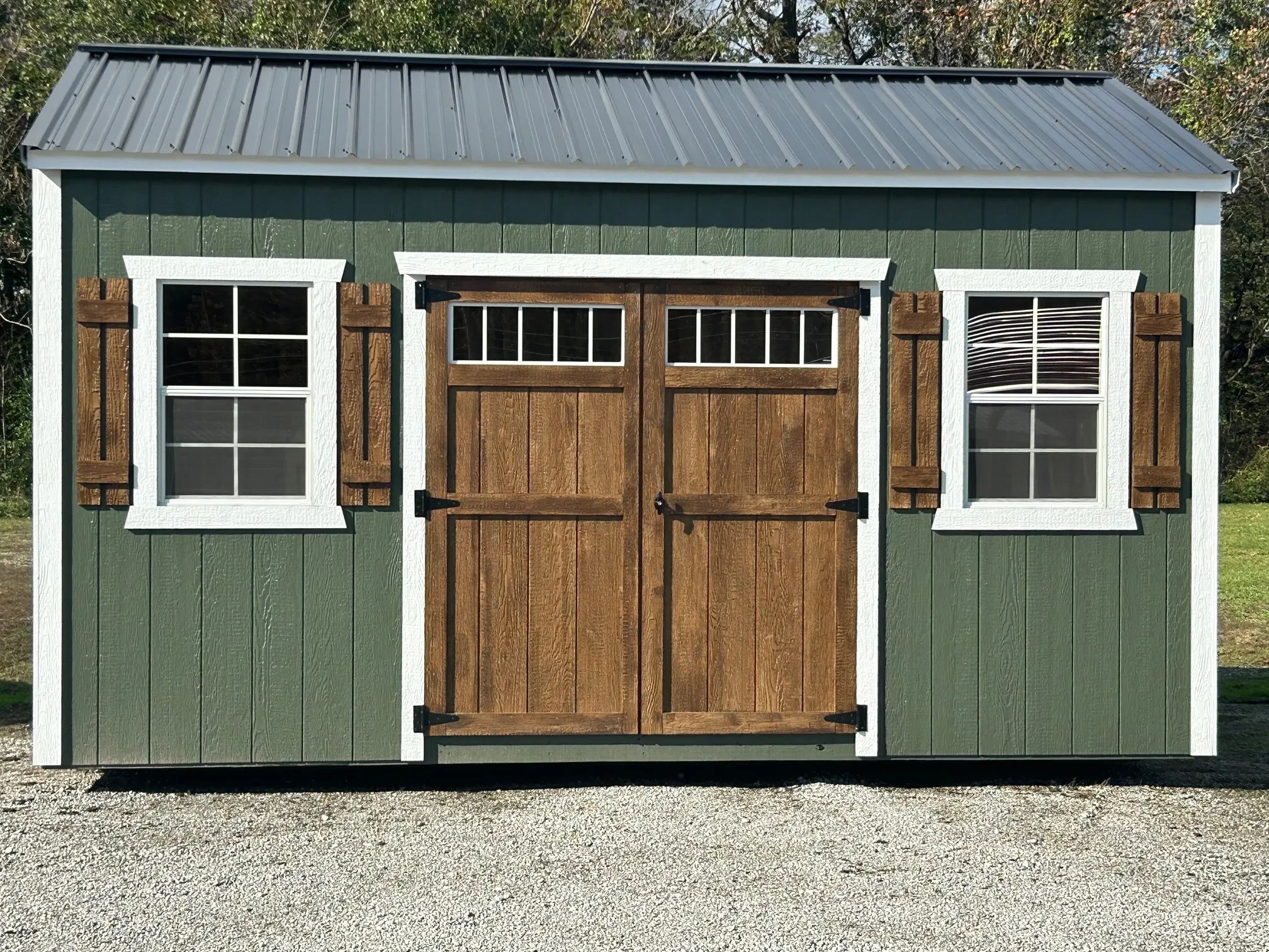 a green garden shed with stained doors and shutters with two windows and transom windows on the double doors