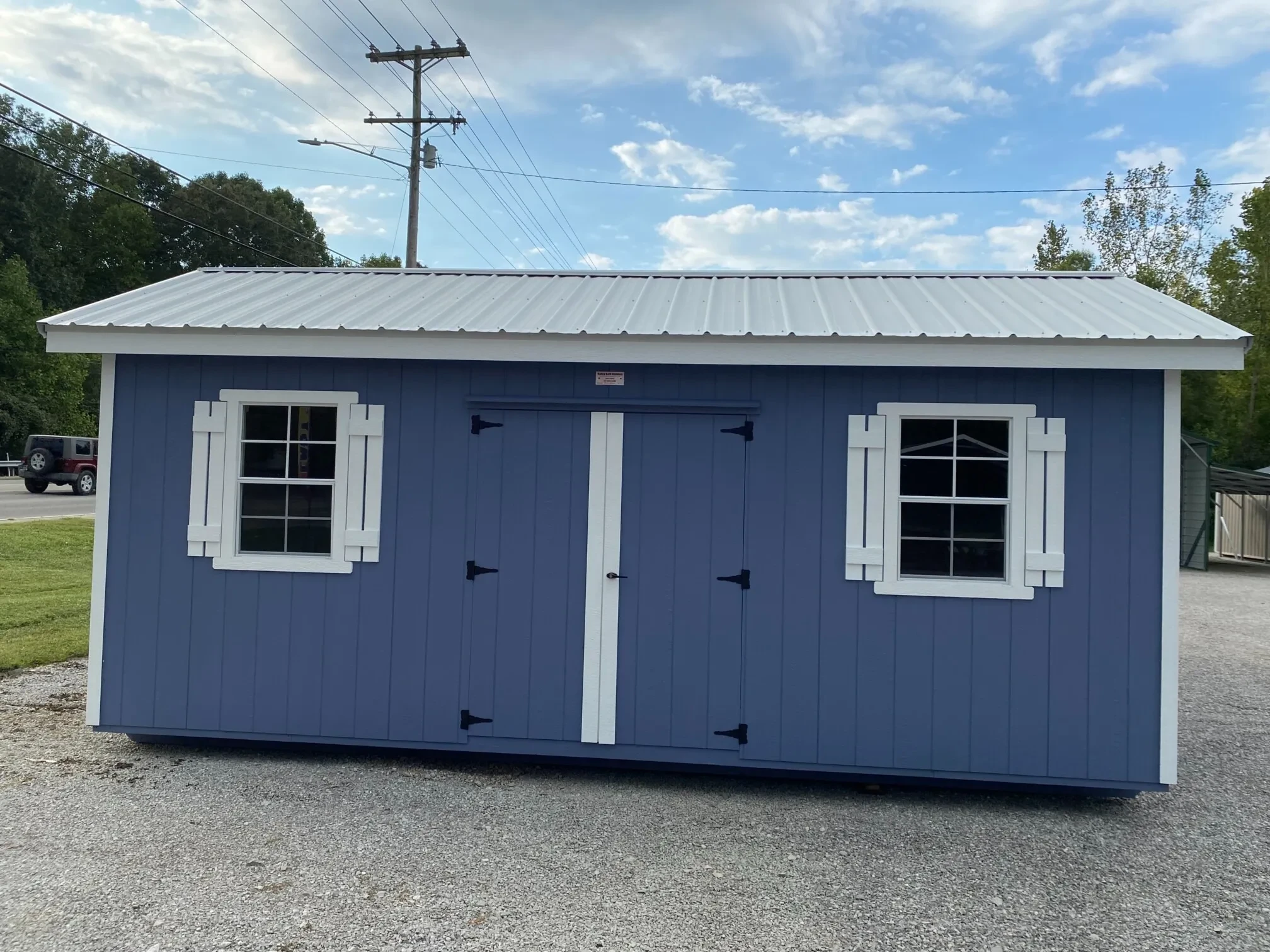 A blue garden shed with windows and shutters and an overhang