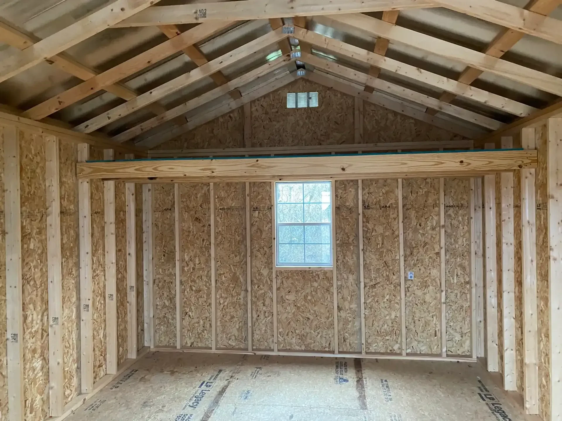 inside a wood shed showing a loft and a 2x3 window along the back wall