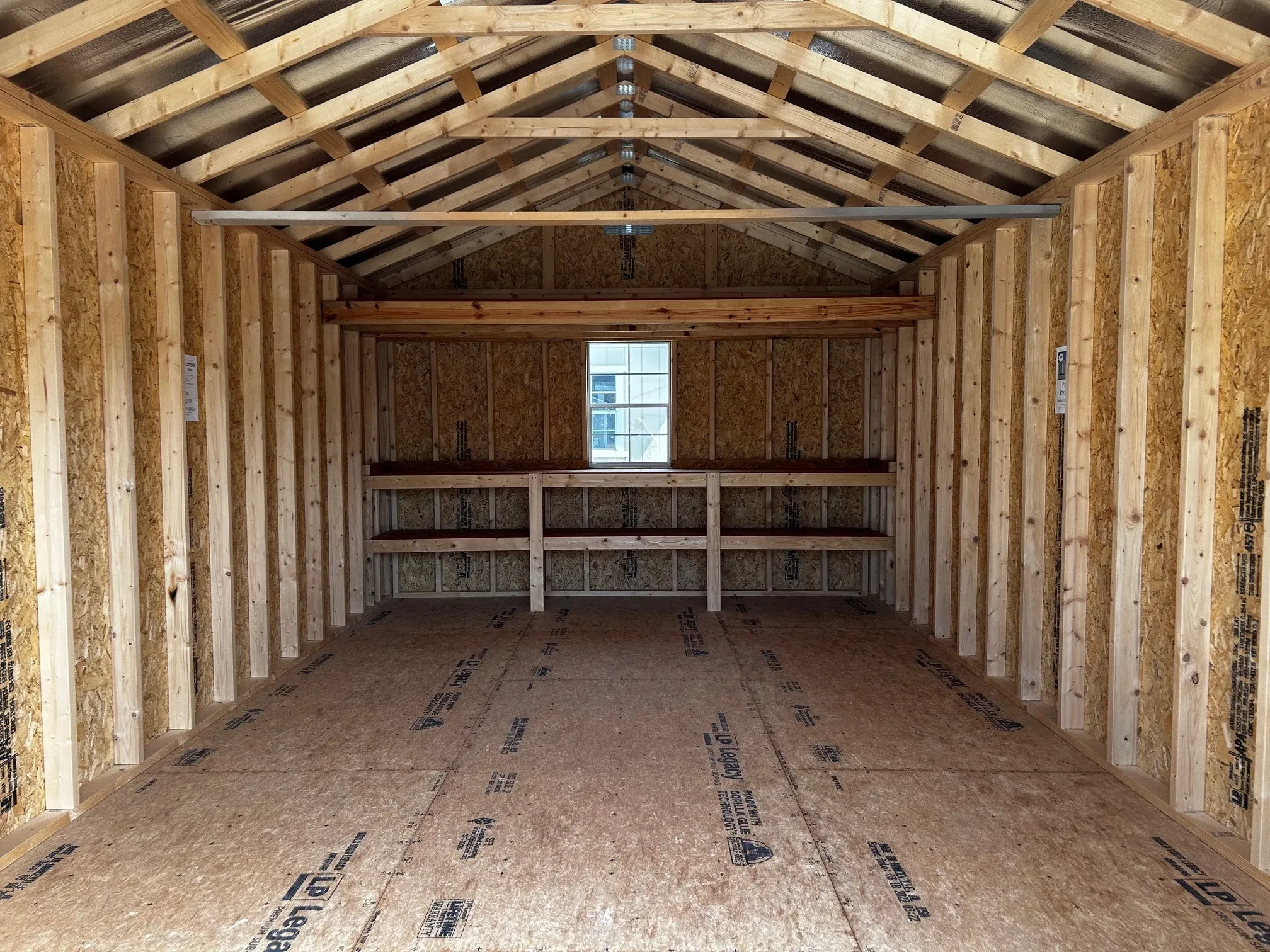 The inside of a wood shed showing double shelves, a loft, and a 2x3 window along the back wall