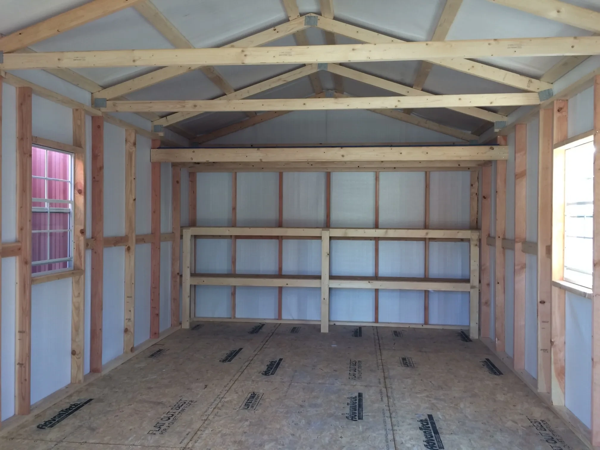 the inside of a metal shed with a window on each wall and double shelves and a loft on the back wall