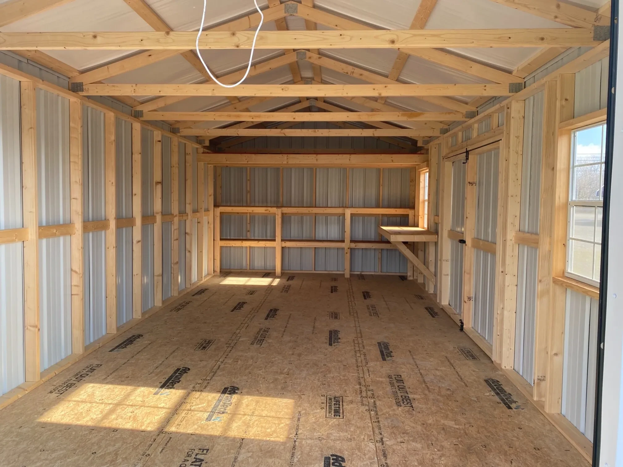 inside a metal garage with double shelves a workbench and windows