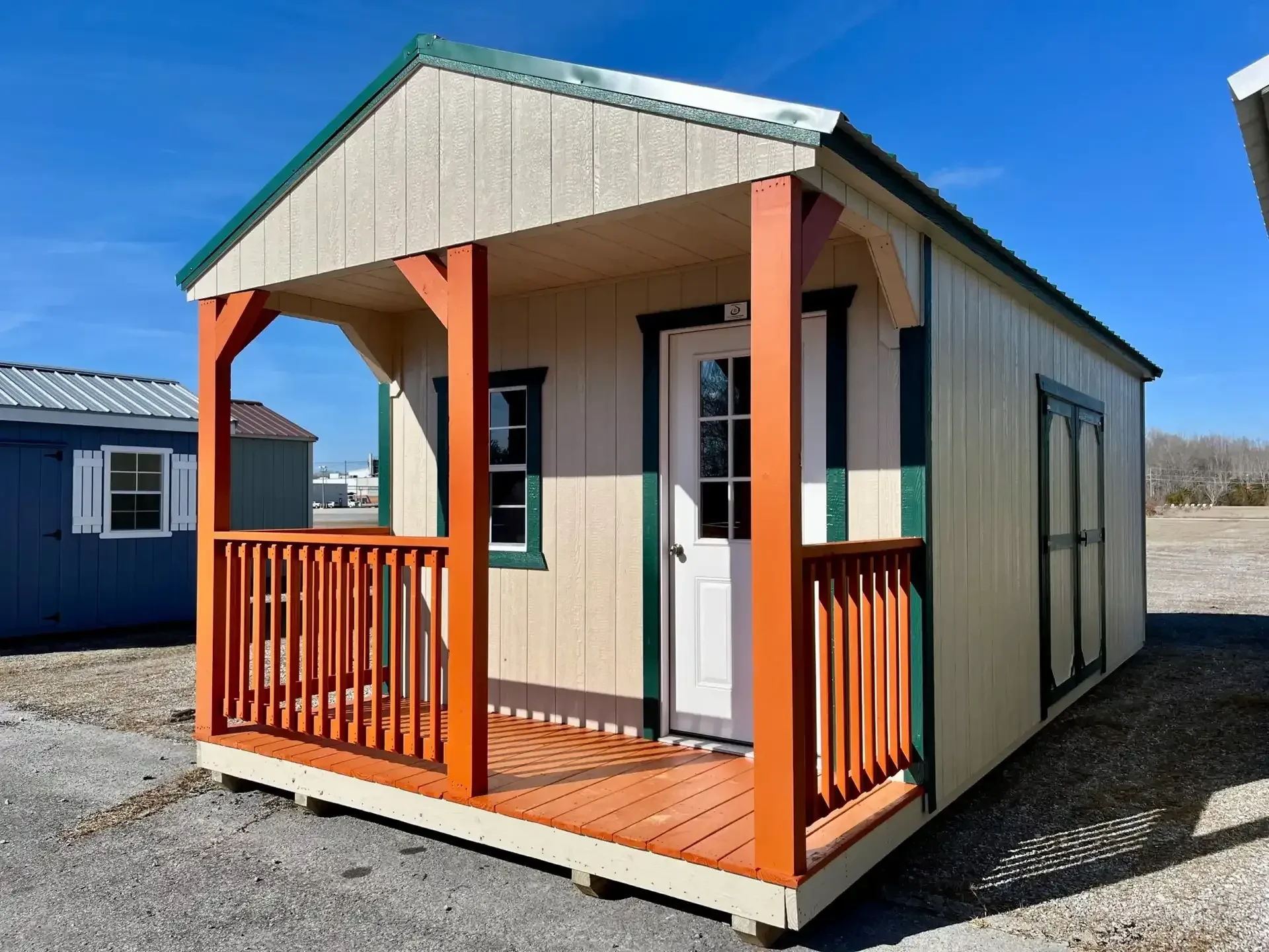 the corner view of a wood shed with an orange porch and green trim