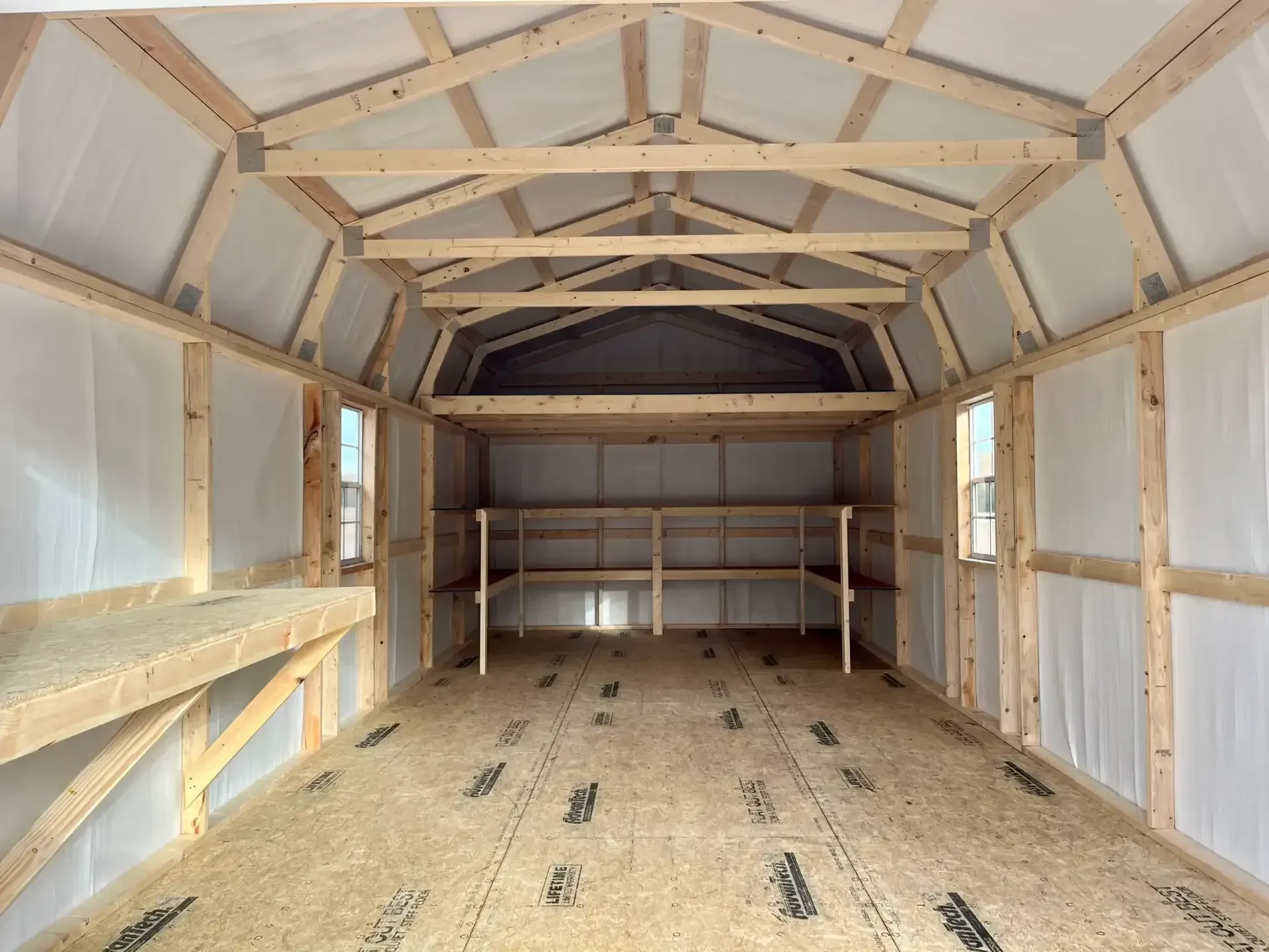 the inside of a large metal lofted barn that is fully insulated showing double shelves, lofts, a workbench and windows