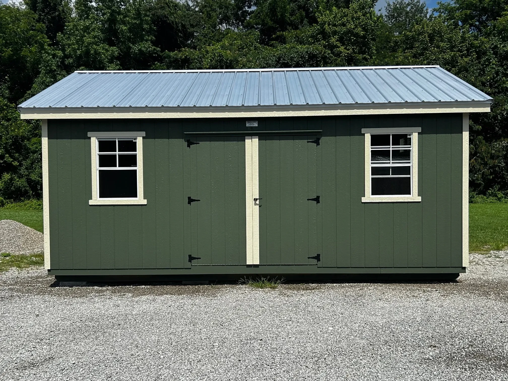 the front of a green shed with double doors and windows and an overhang all around the shed