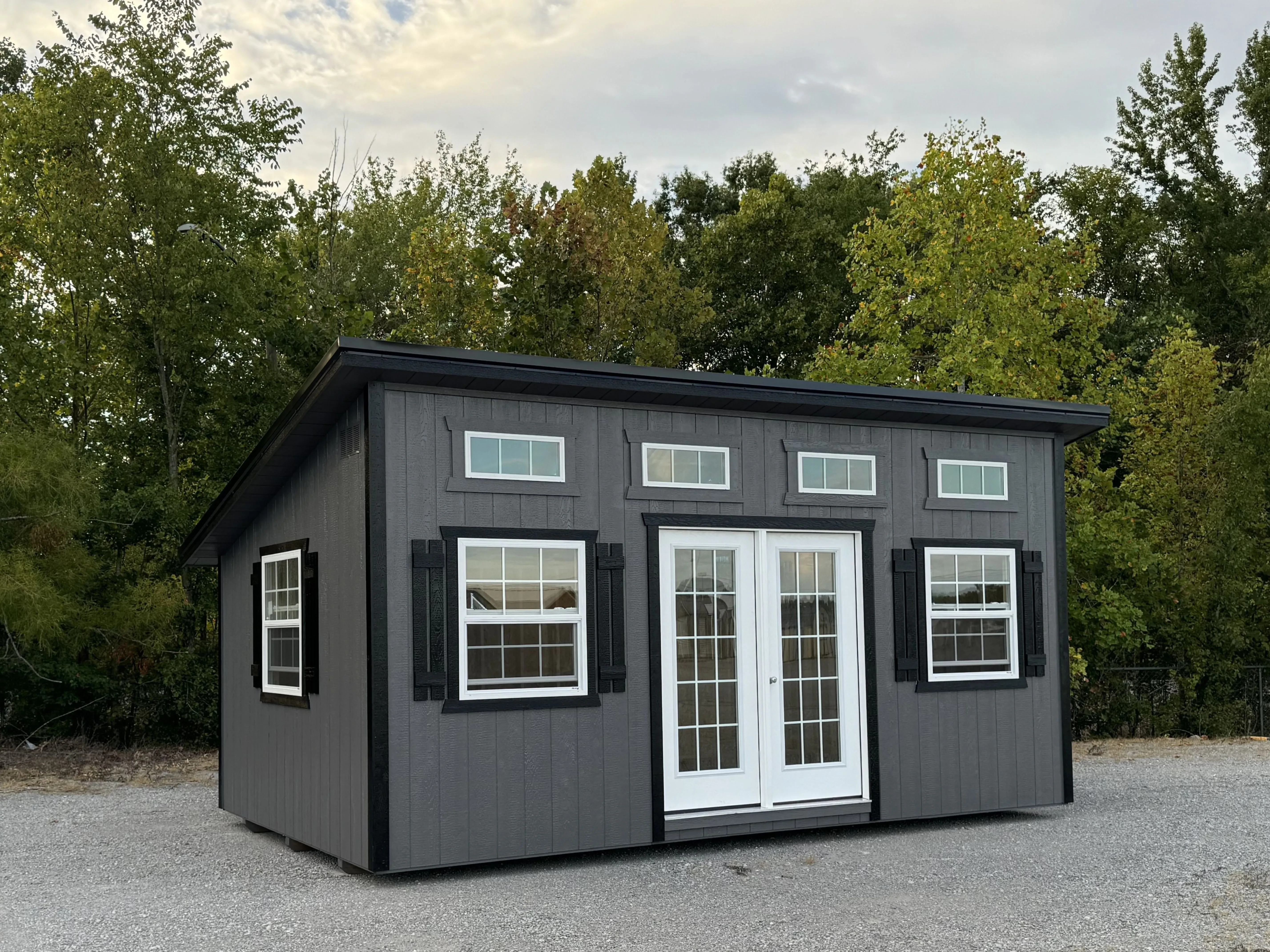 Gray and black studio shed with trees.