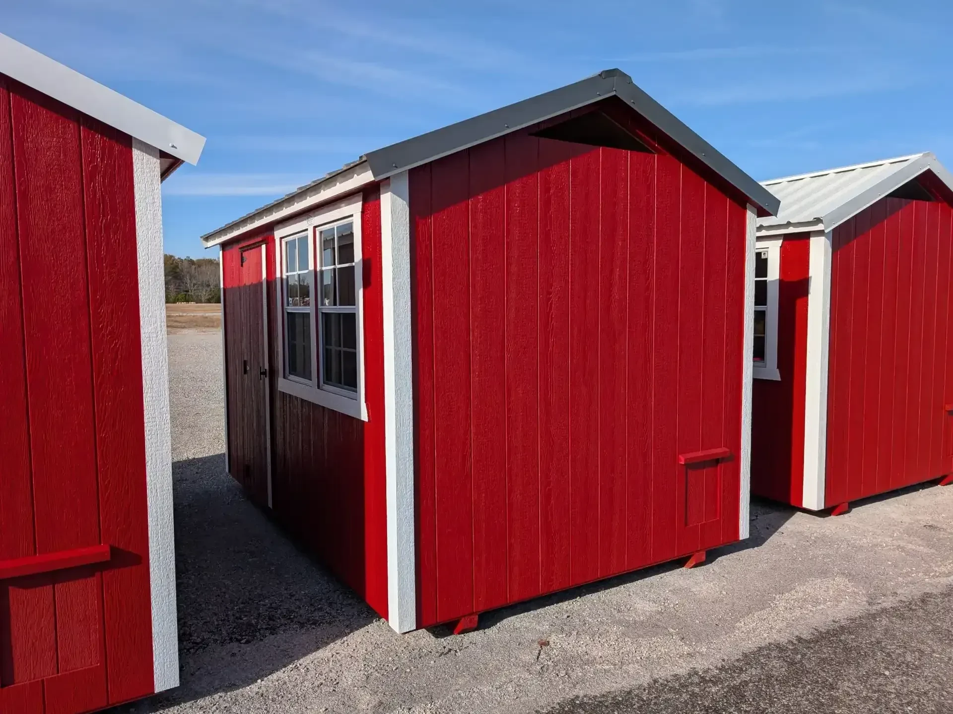 The corner front view of a red chicken coop with white trim and two windows