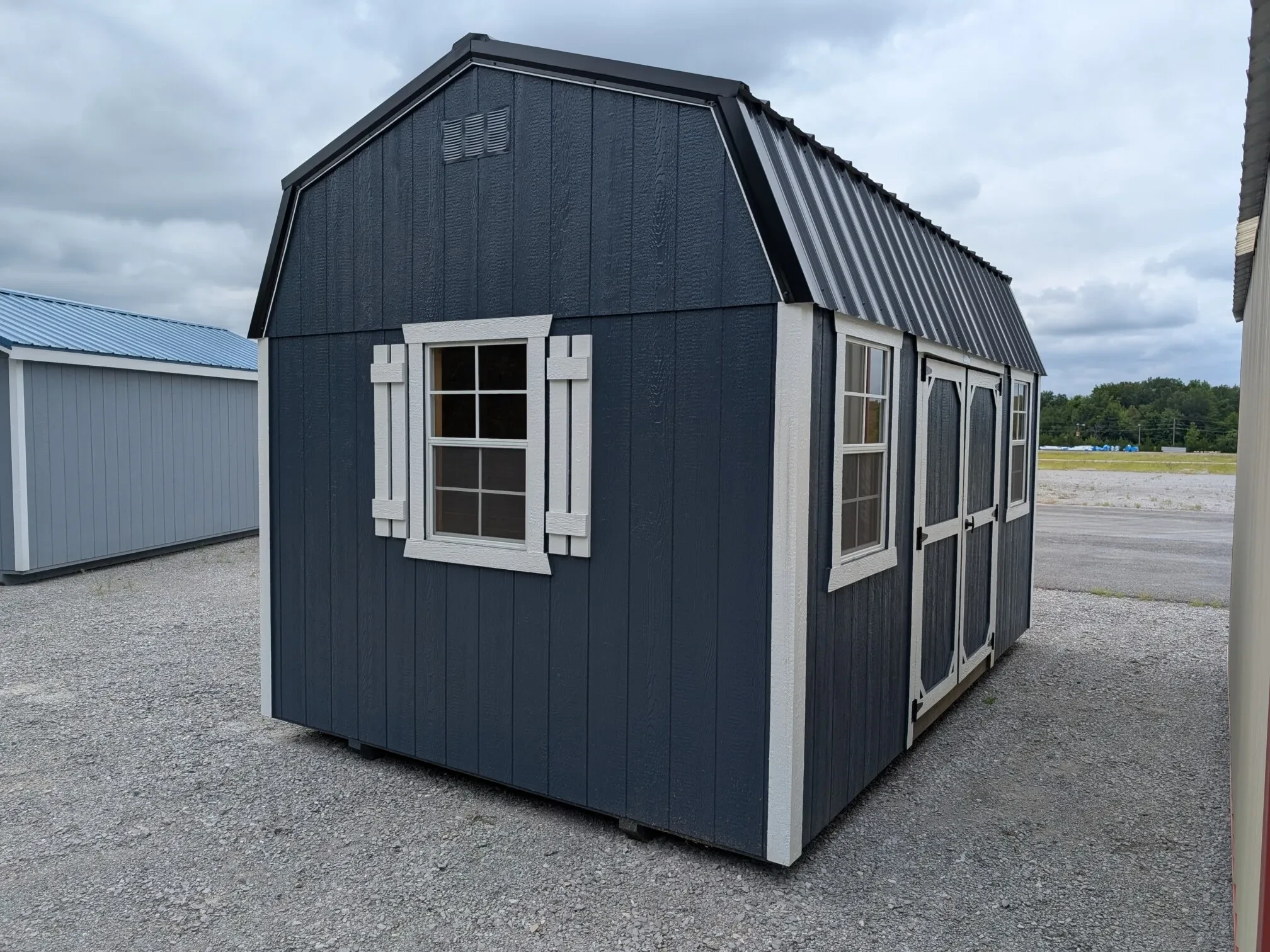 a blue side lofted barn with white trim and windows with shutters