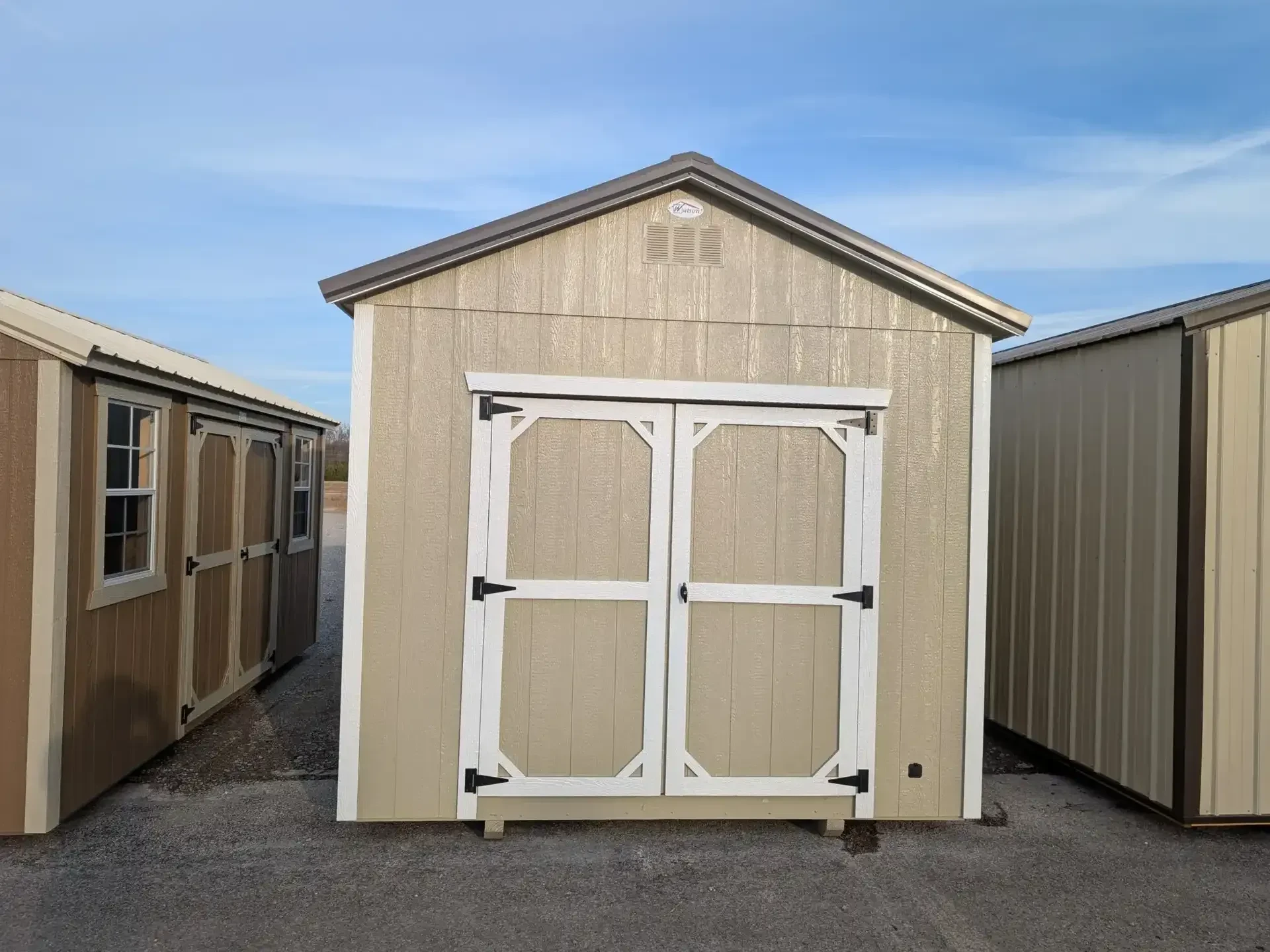 the front of a wood shed painted light stone with white trim