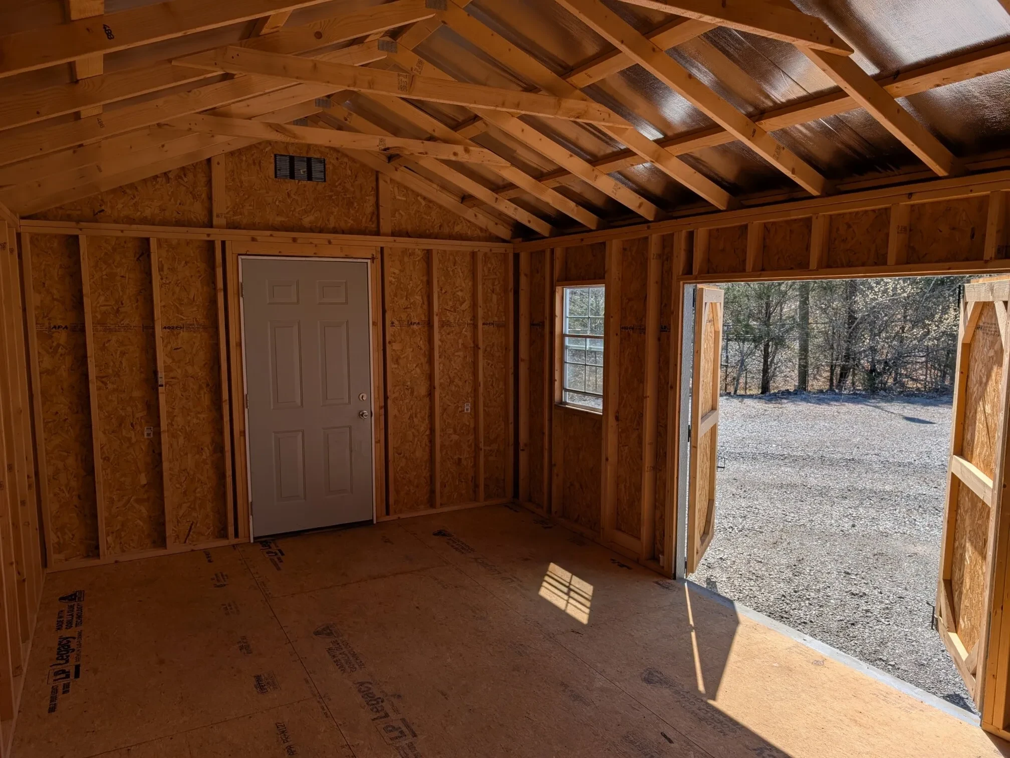 inside a wood shed with a walk-in door, a window, and the double doors open