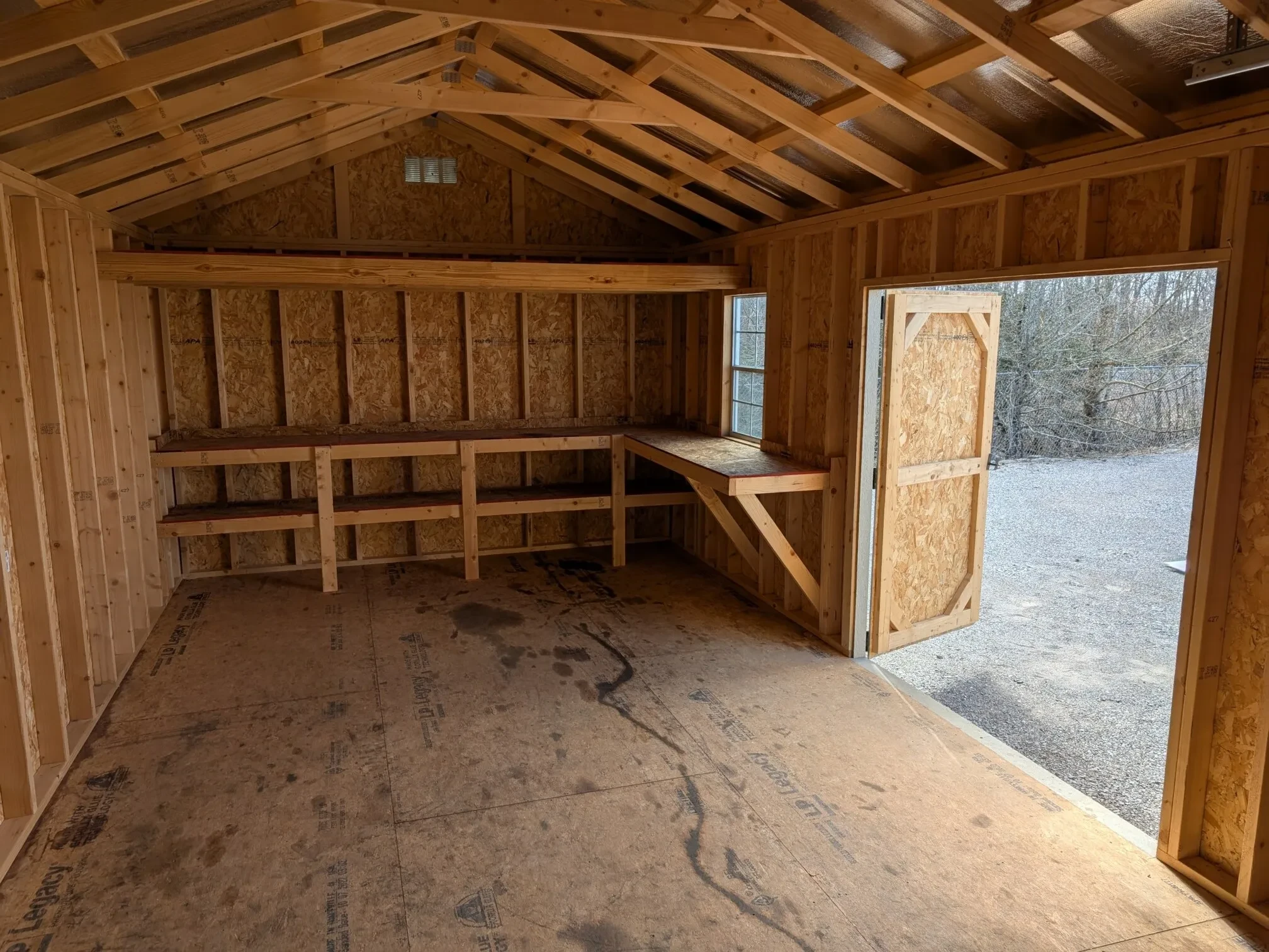 inside a wood garage shed with double shelves, a loft, a workbench and the double doors wide open