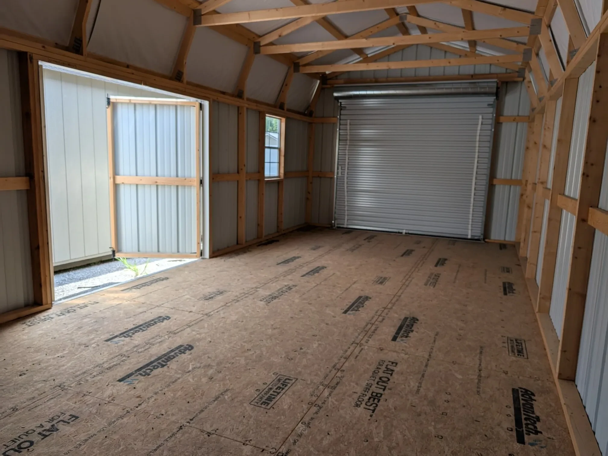 inside a lofted garage looking at the garage door which is closed but the double doors are open