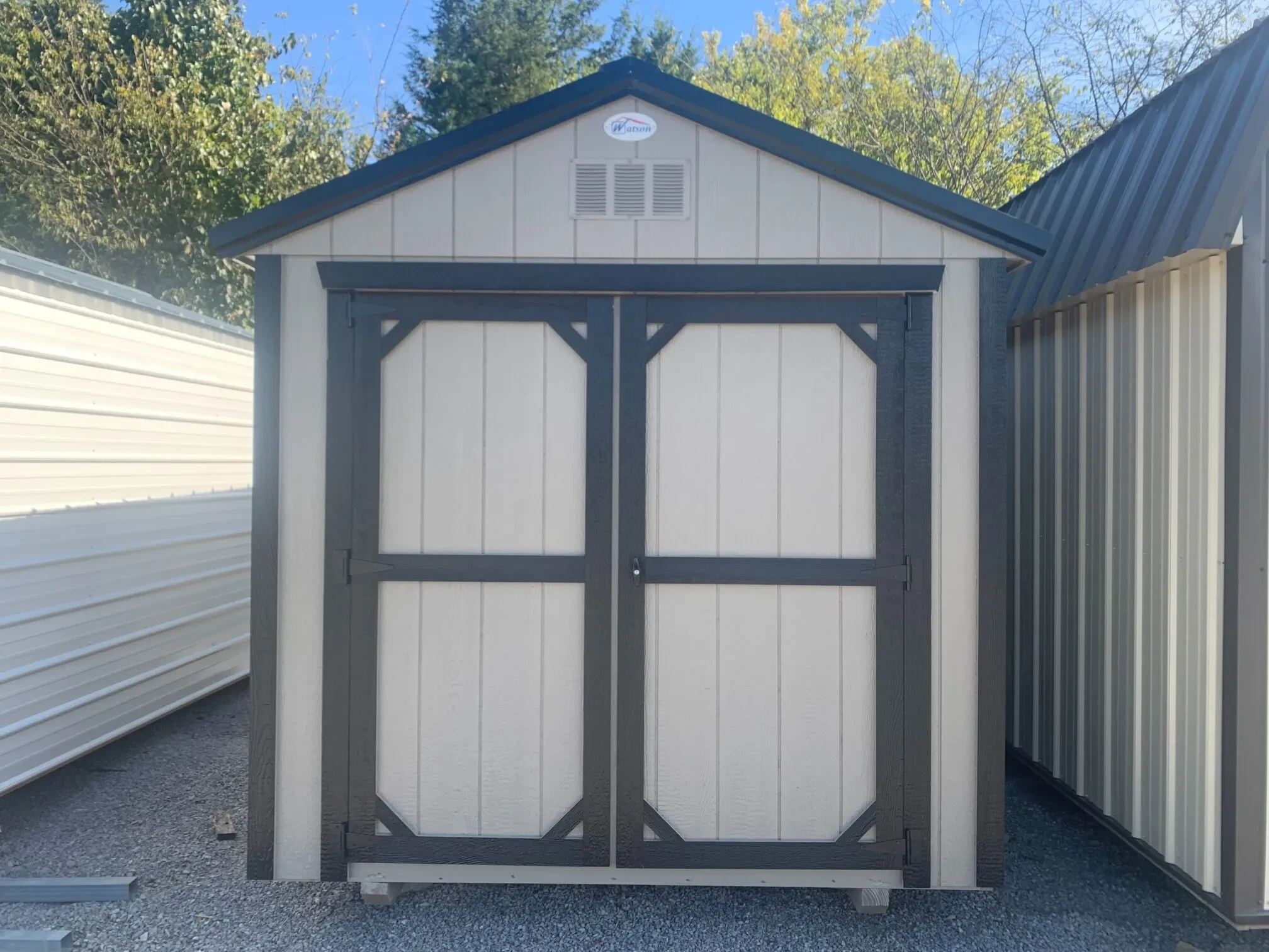 a wood shed with double doors and it is colored clay with black trim