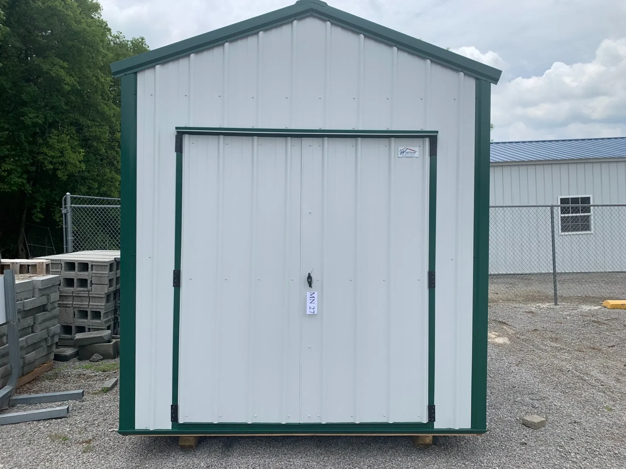 a white metal shed with green trim and double doors