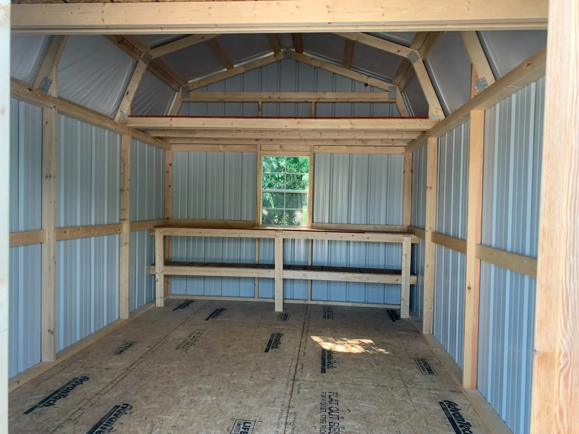 inside a metal shed with a loft, double shelves, and a window on the back wall