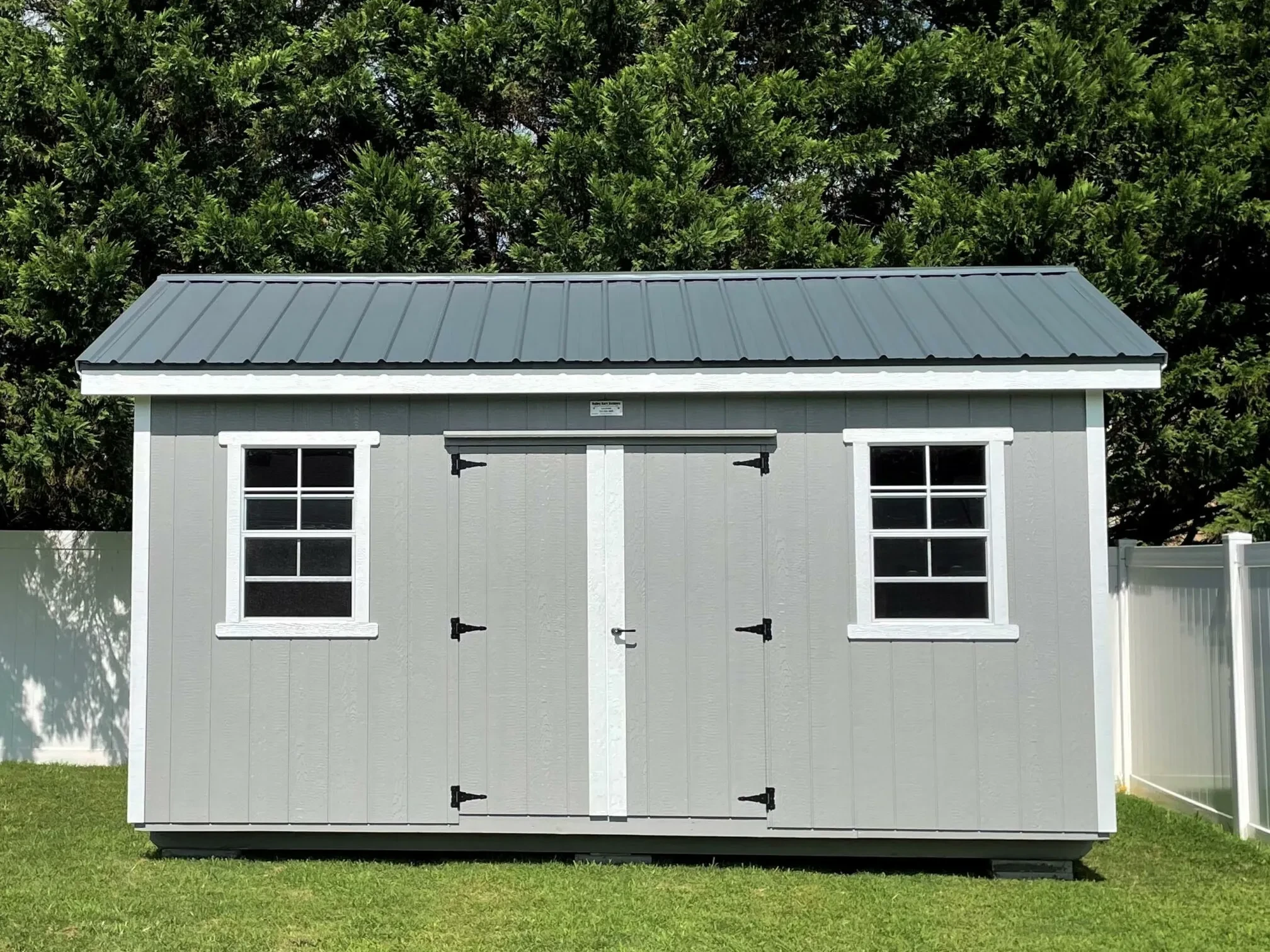 a garden shed with double doors and a window on each side of the doors with gray siding