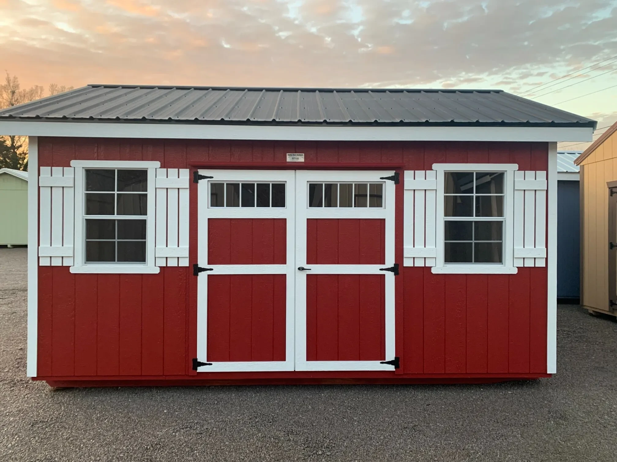red garden shed with double doors with transom windows in them, along with two 2x3 windows with white shutters