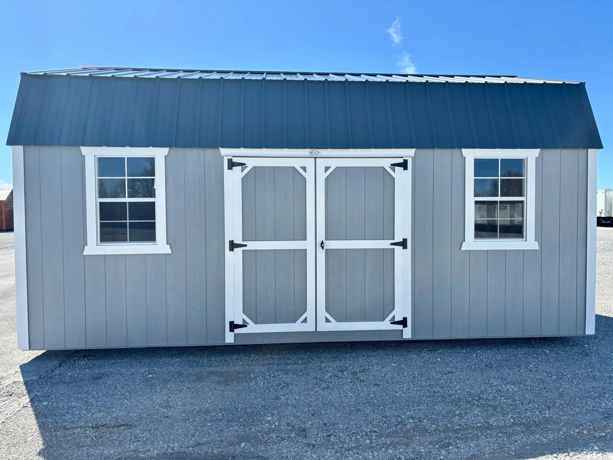 a light gray side lofted barn with double doors and two windows